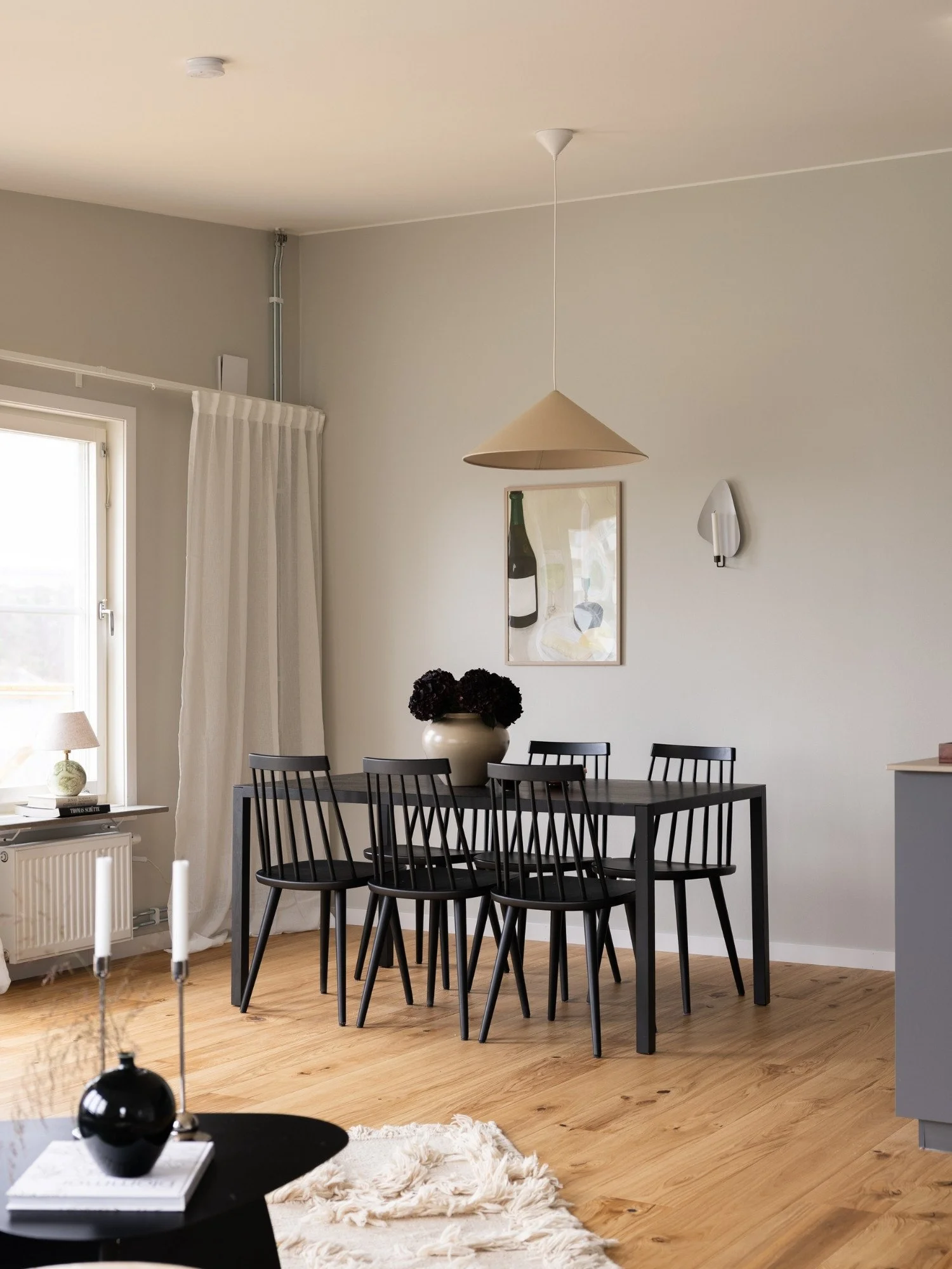 Stylad matplats med svart matbord och sex svarta pinnstolar, taklampa, blommor, tavla och väggljusstake