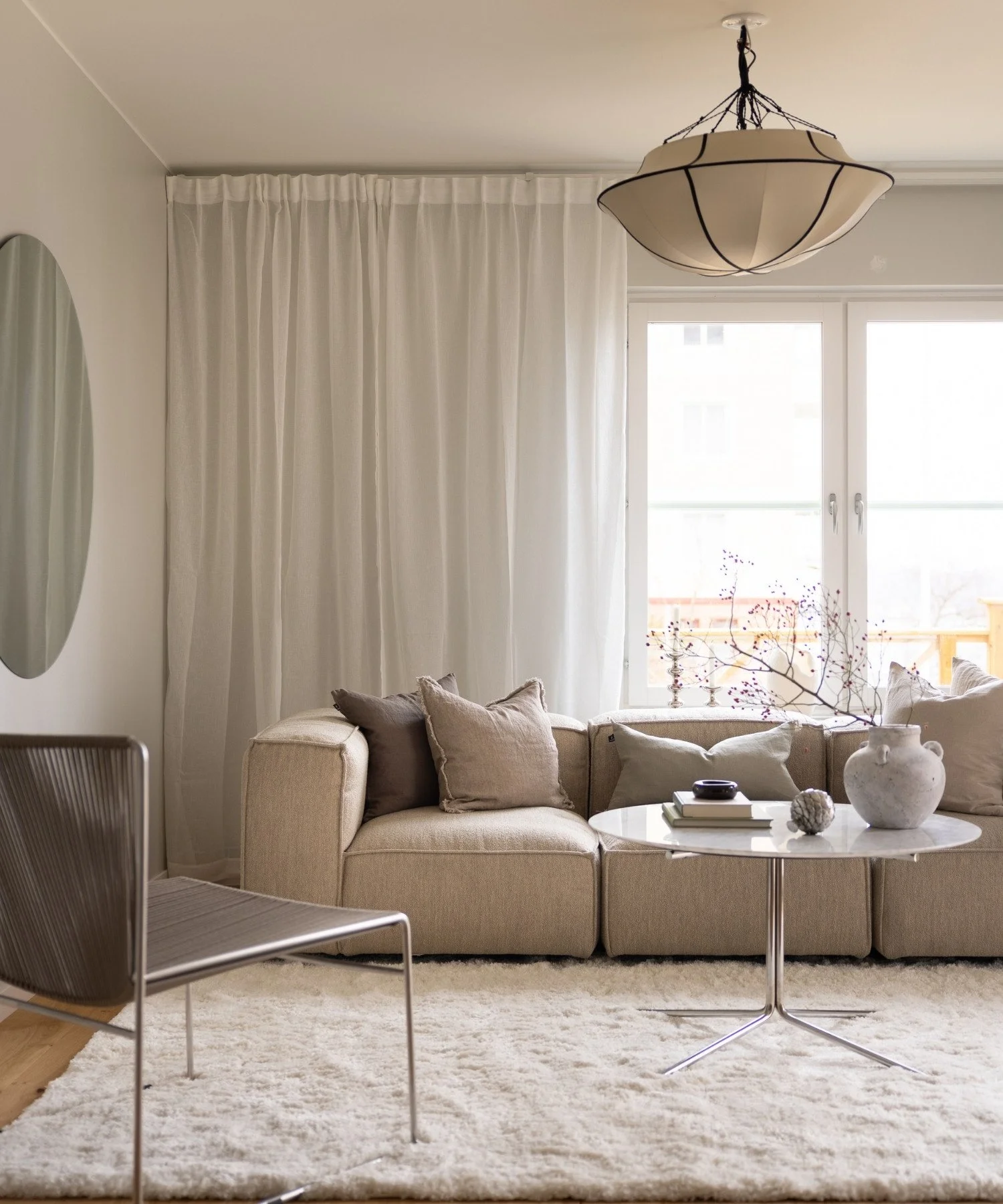 Skandinaviskt och neutralt vardagsrum med modern soffa, stol, bord och belysning samt genomtänkta inredningsdetaljer