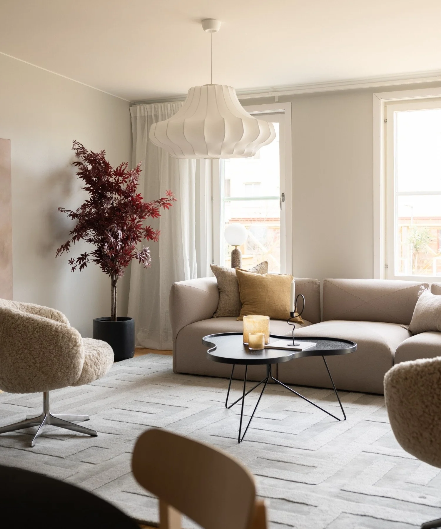 Inredningsprojekt med ljust och luftigt vardagsrum inrett med fåtöljer i fårskinn, modern soffa, matta, bord, belysning, mjuka textilier och grönska