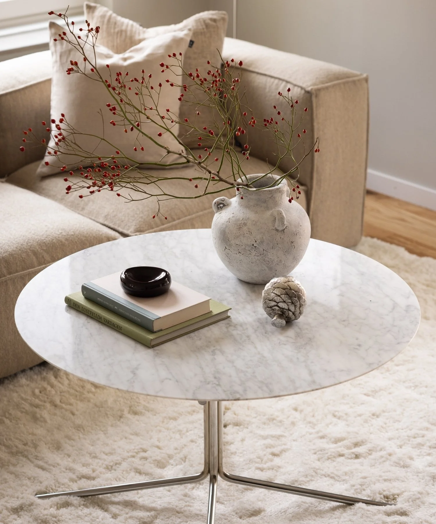 Stilleben på soffbord i marmor och stål med böcker, ljus rustik vas med kvist och dekorativa detaljer