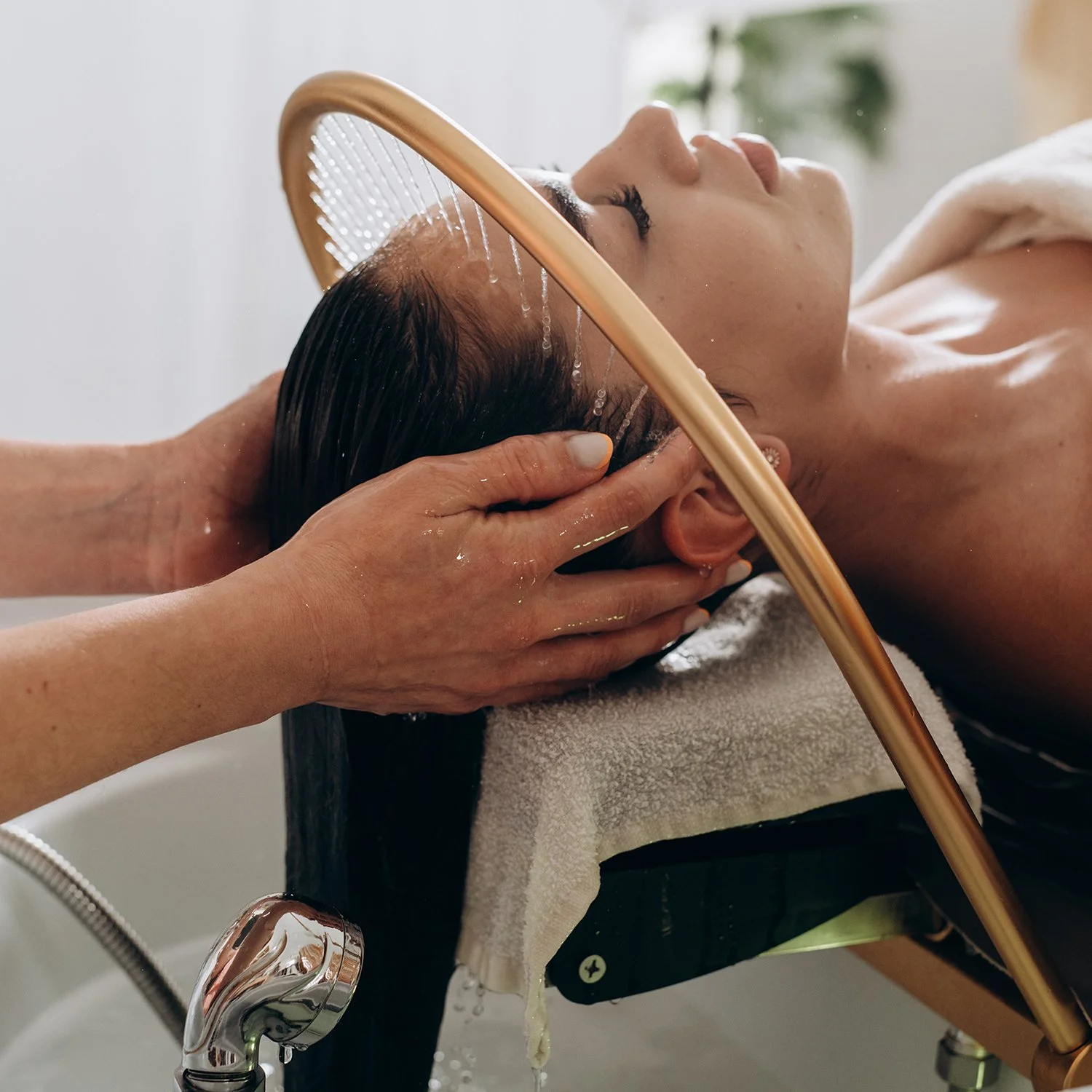 A woman receives a head massage in with water falling from the shower of head spa equipment at Renewed Life Esthetics and Head Spa.