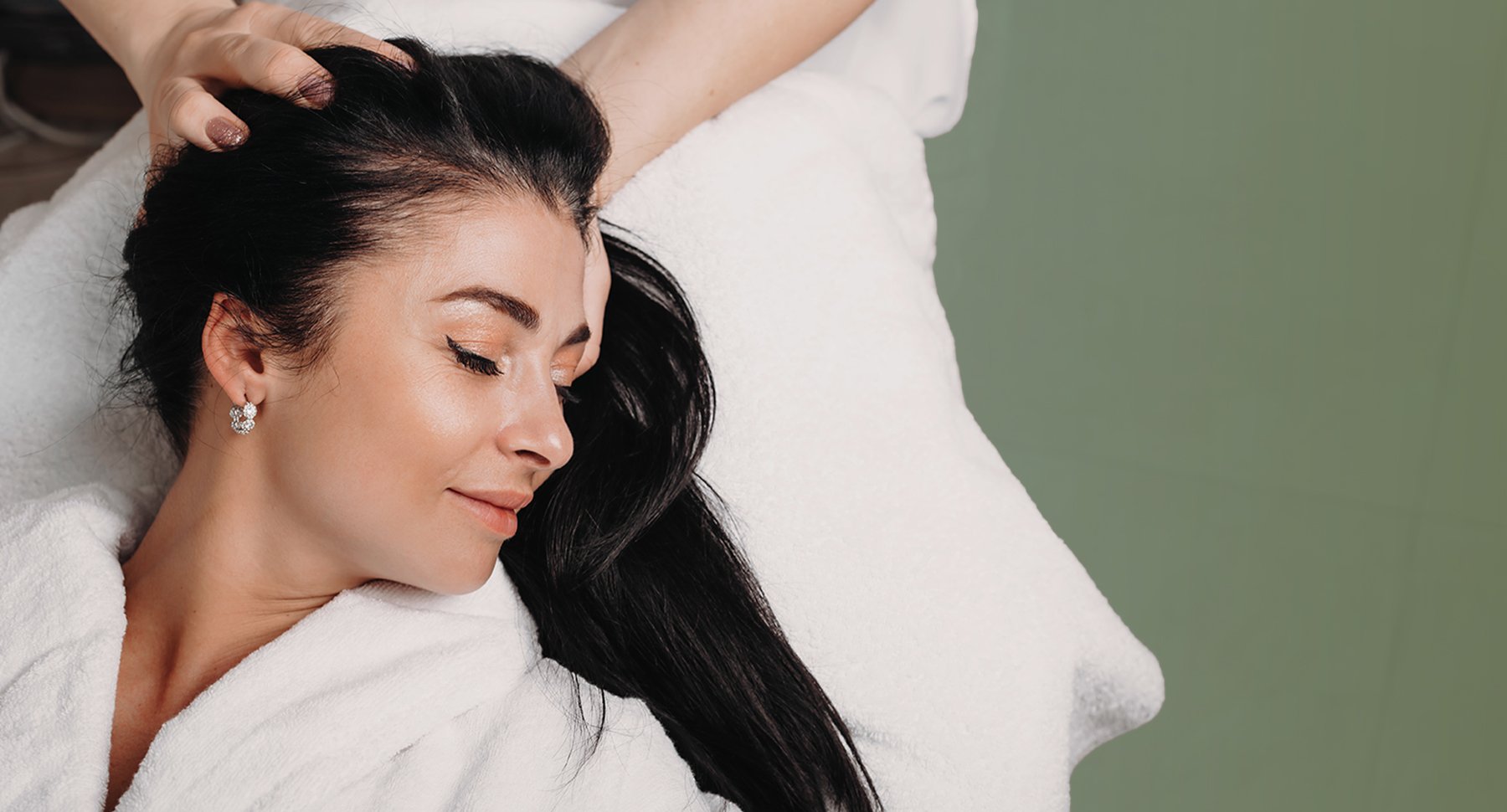 A woman receiving a scalp massage from a therapist, lying on a white towel eyes closed, About Renewed Life Esthetics and Head Spa.