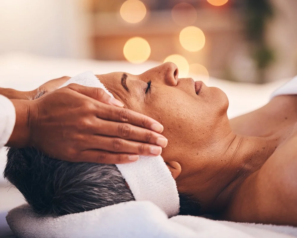 A woman receives a facial massage with masseuse gently presses her temples at Renewed Life Esthetics and Head Spa.