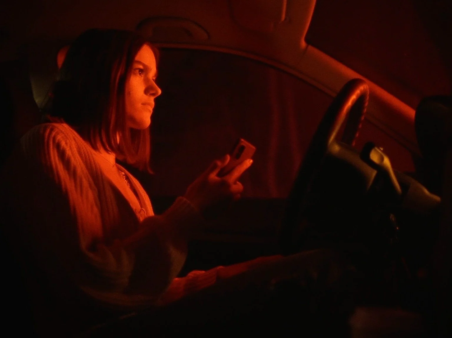 Frau sitzt in einem Auto bei schwachem Licht und schaut auf ihr Handy.