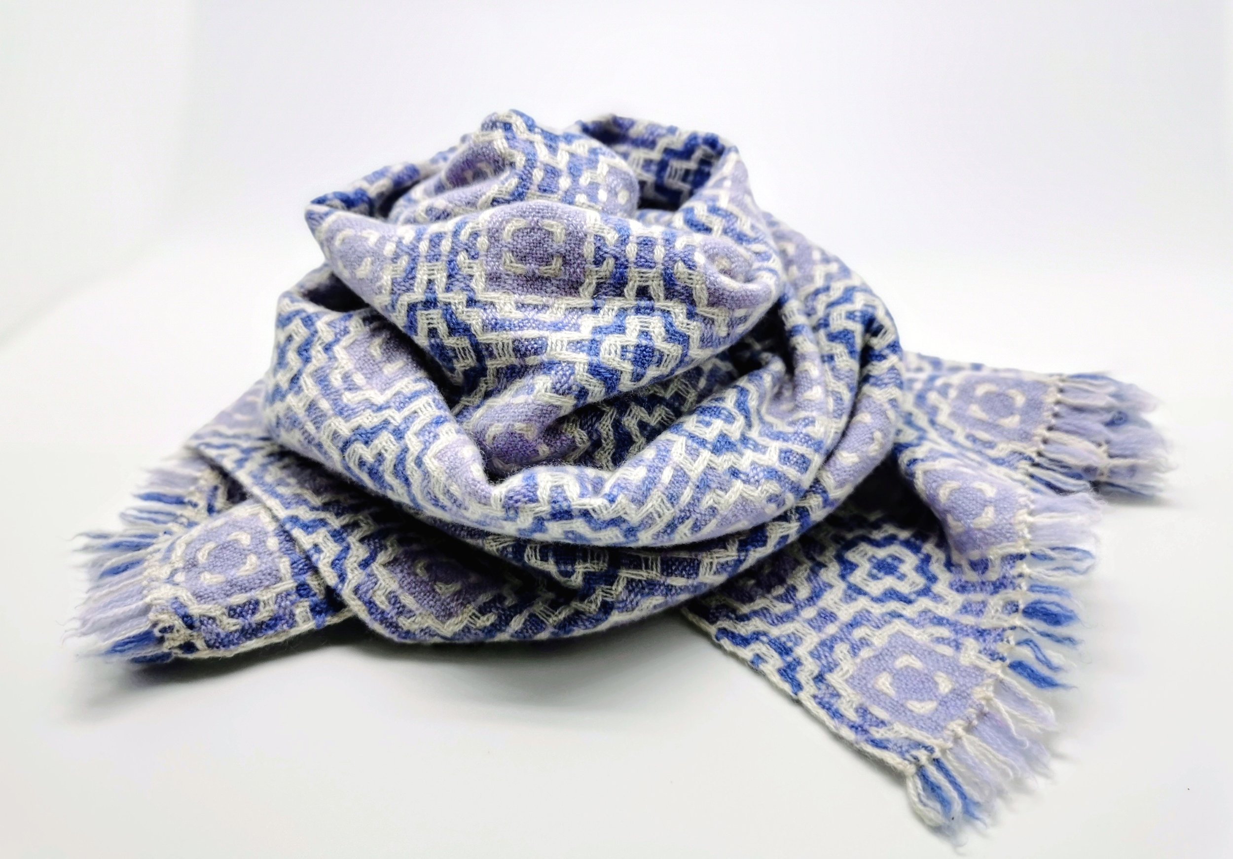 Écharpe Lilas en pur cachemire roulée sur elle-même, motif géométrique en dégradé de violet foncé et violet pâle sur fond blanc, courtes franges libres visibles
