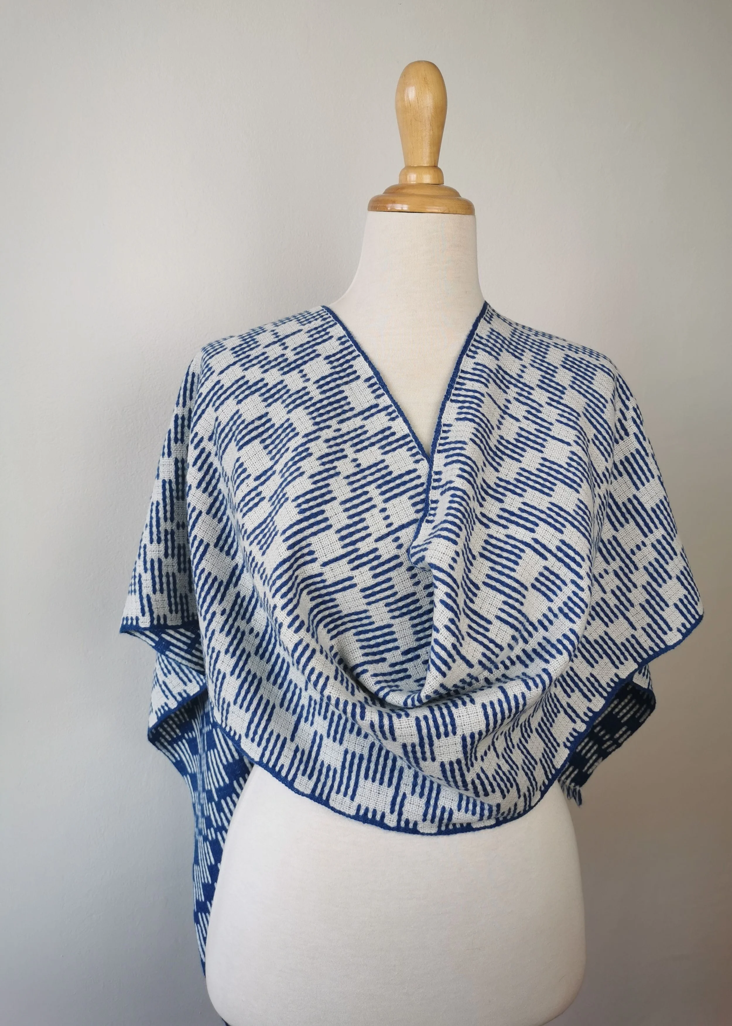 Écharpe Sillage drapée sur les épaules d'un mannequin : face écrue à motif de tirets bleu cobalt, fine lisière bleue