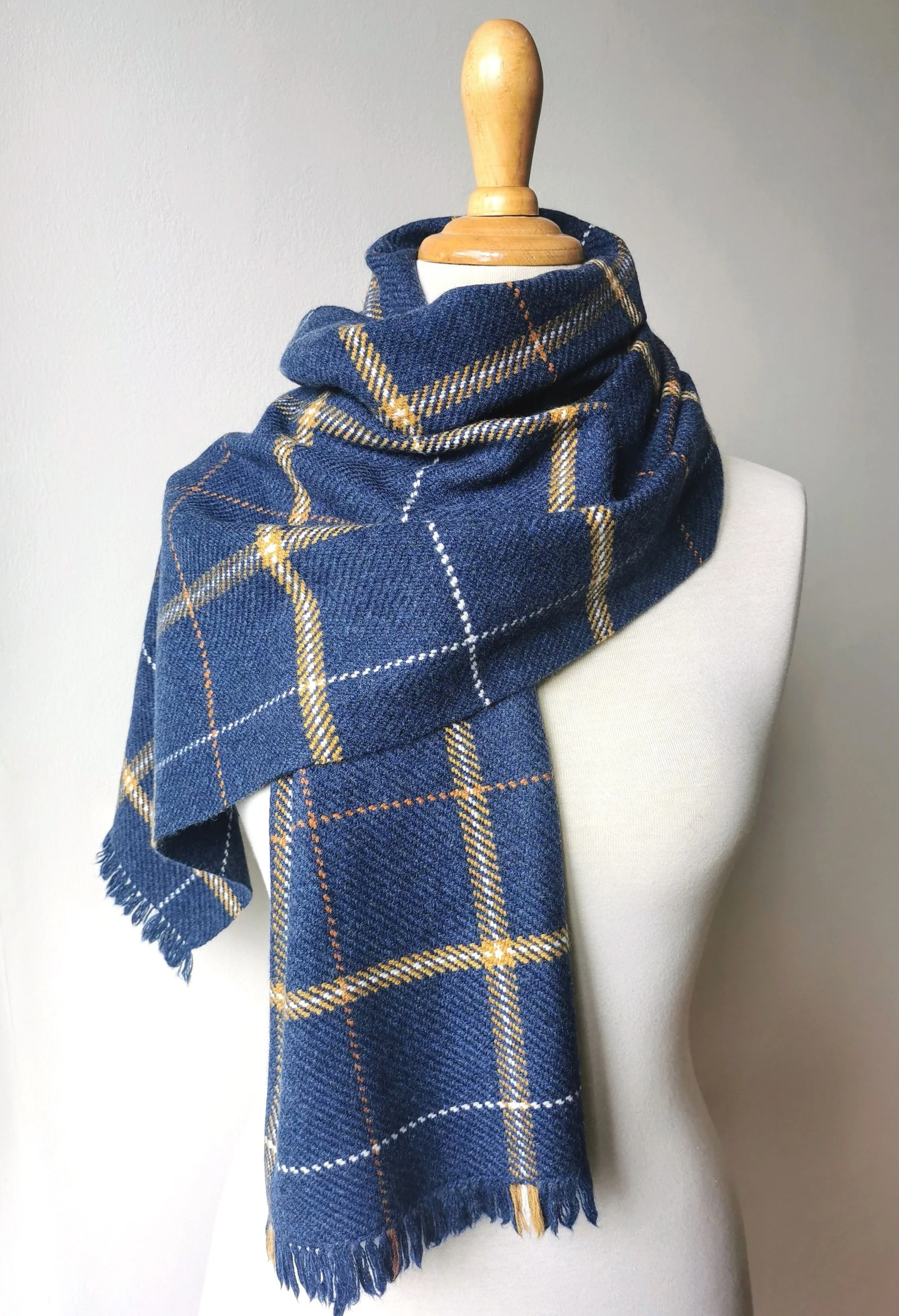Écharpe Loch en laine mérinos enroulée autour du cou d'un mannequin, motif de carreaux bleu profond avec lignes écrues, orangées et dorées, courtes franges libres en bas