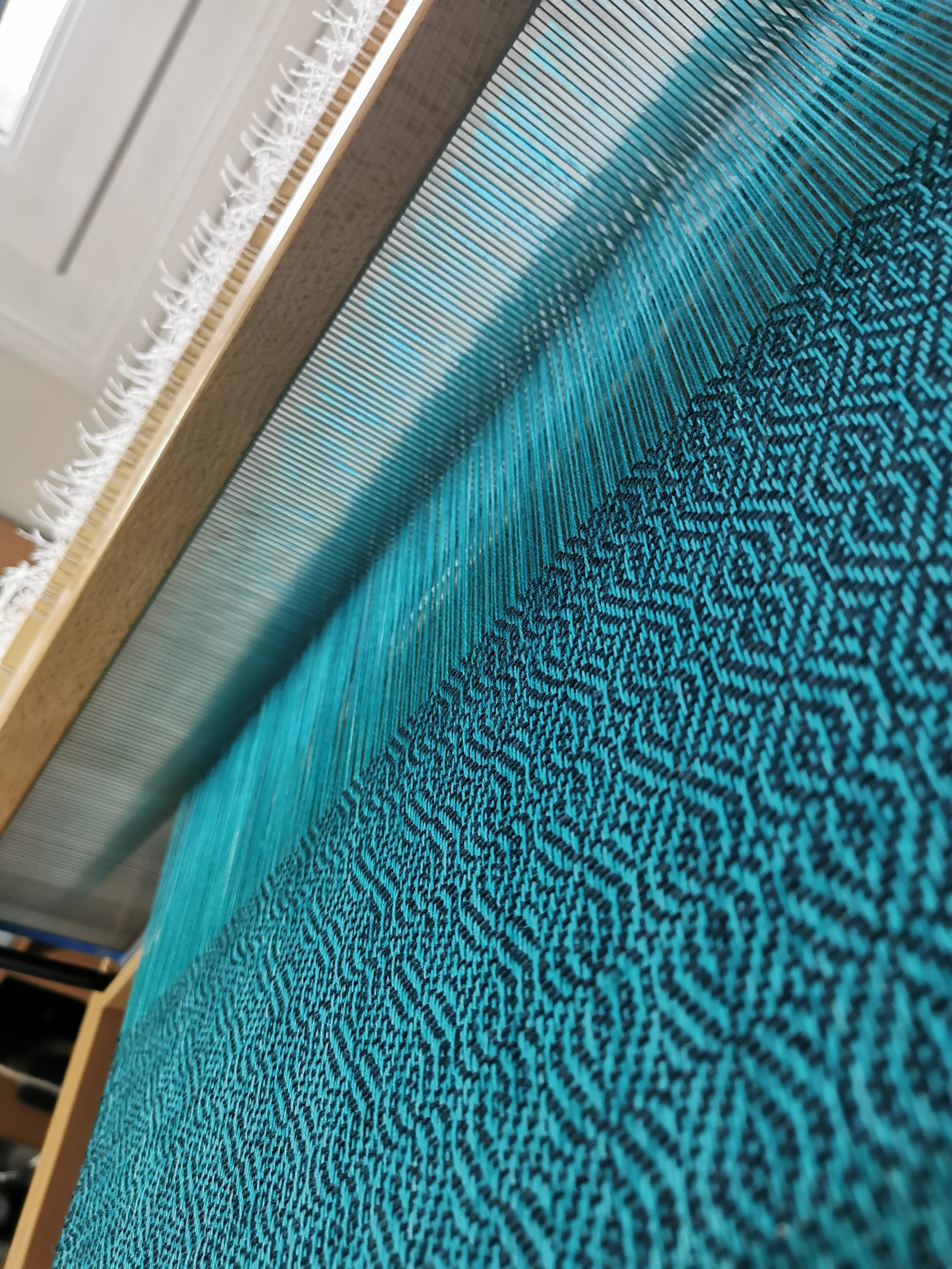 Écharpe Topaze en cours de tissage sur métier à bras, mérinos turquoise et trame noire en cachemire