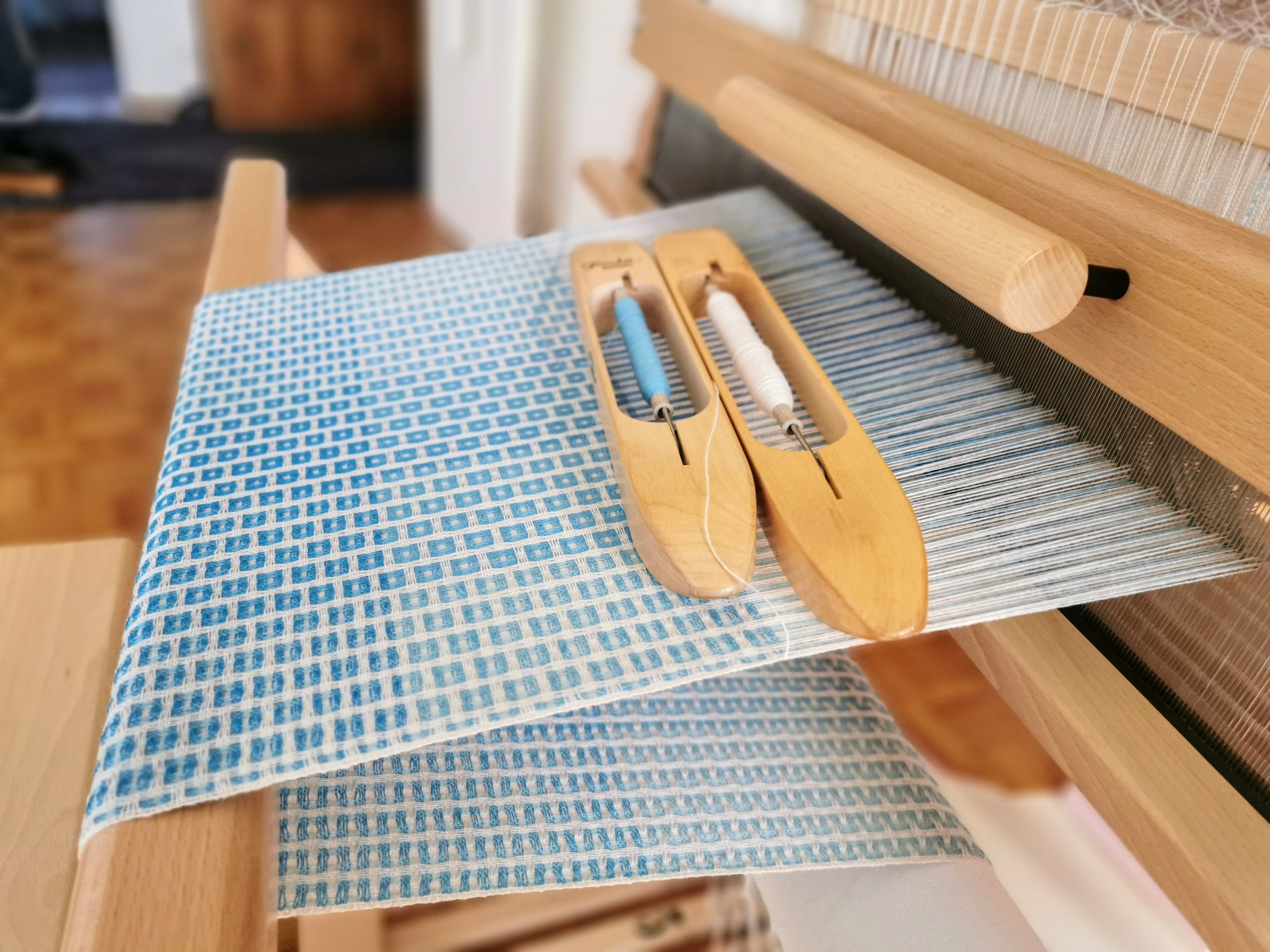 Une machine à tisser en bois avec du fil blanc et bleu sur un tissu à motif carré bleu et blanc.