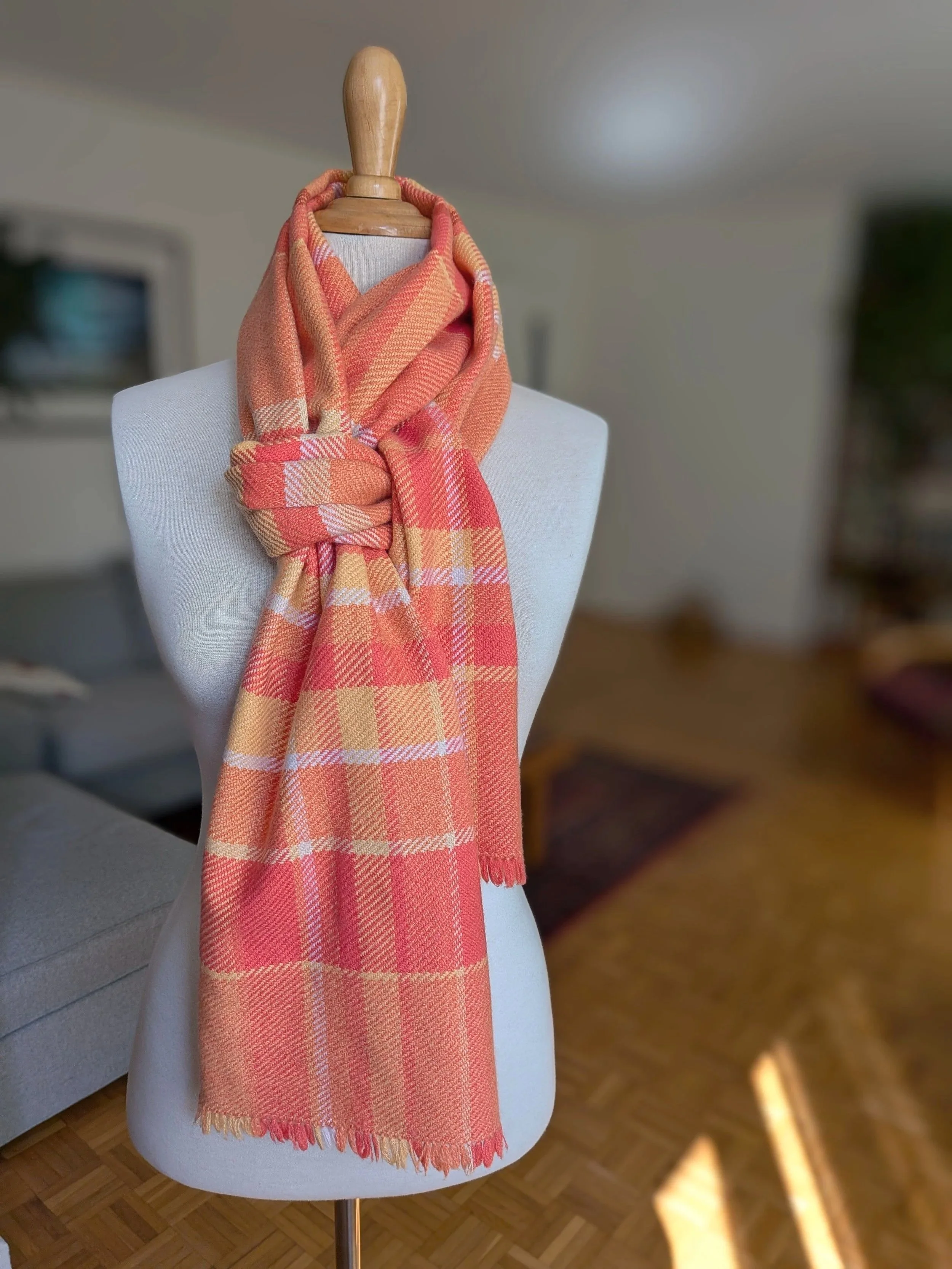 Écharpe Mandarine en pur cachemire nouée autour du cou d'un mannequin, motif de carreaux en nuances d'orange, de corail et de jaune doré, courtes franges libres en bas