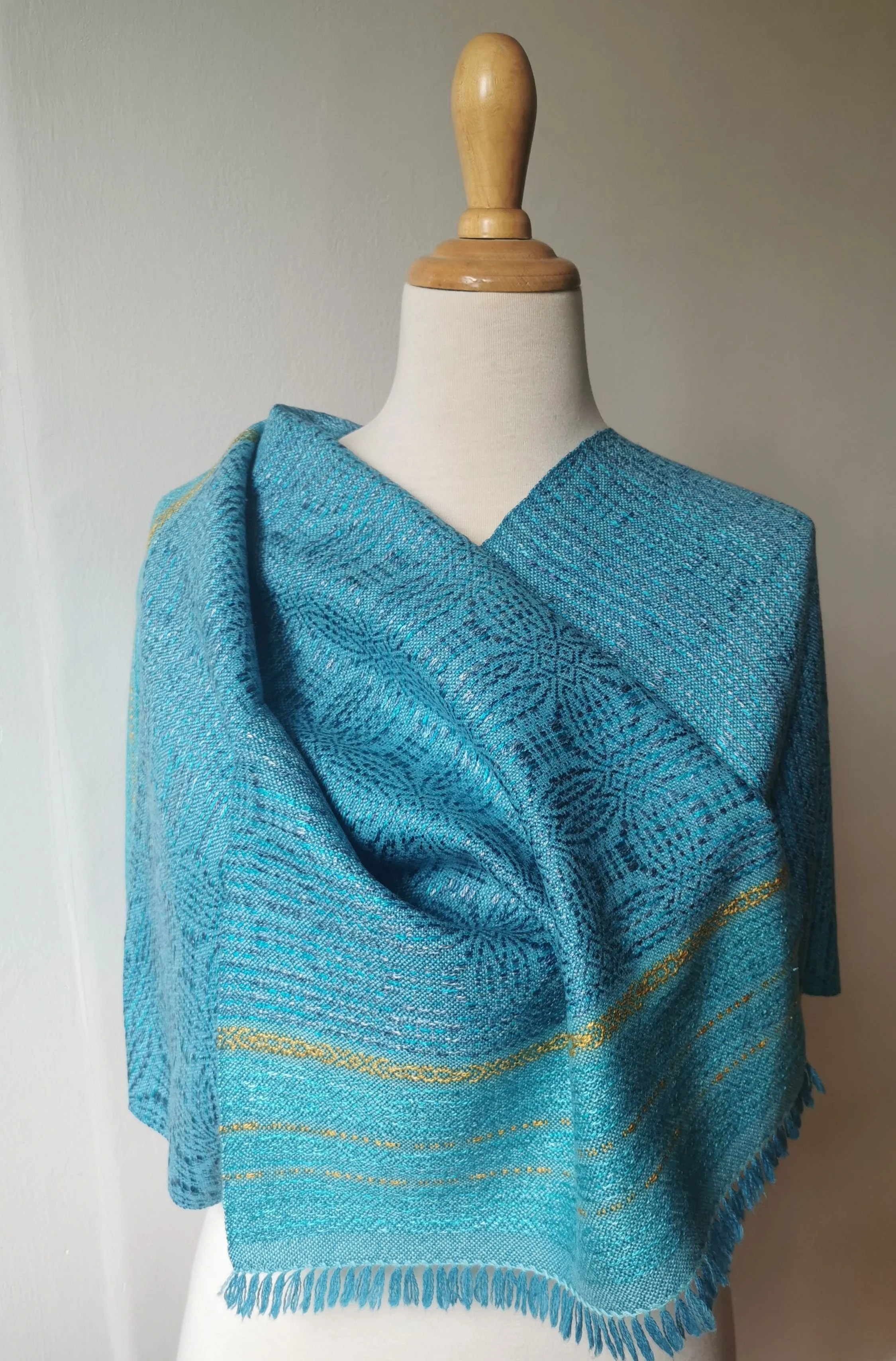 Étole Calypso en cachemire et soie portée en châle croisé sur les épaules d'un mannequin, motif en relief turquoise et bandes dorées