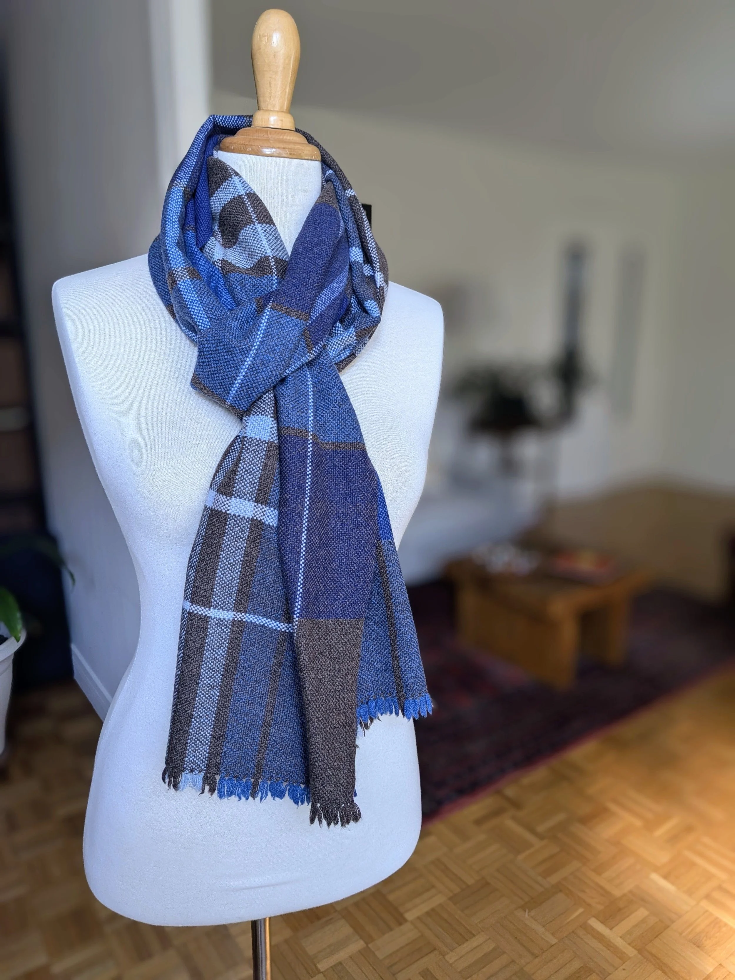 Écharpe Boréal en pur cachemire nouée autour du cou d'un mannequin, un long pan retombant devant, motif de carreaux en camaïeu de bleus, brun profond et blanc, franges visibles