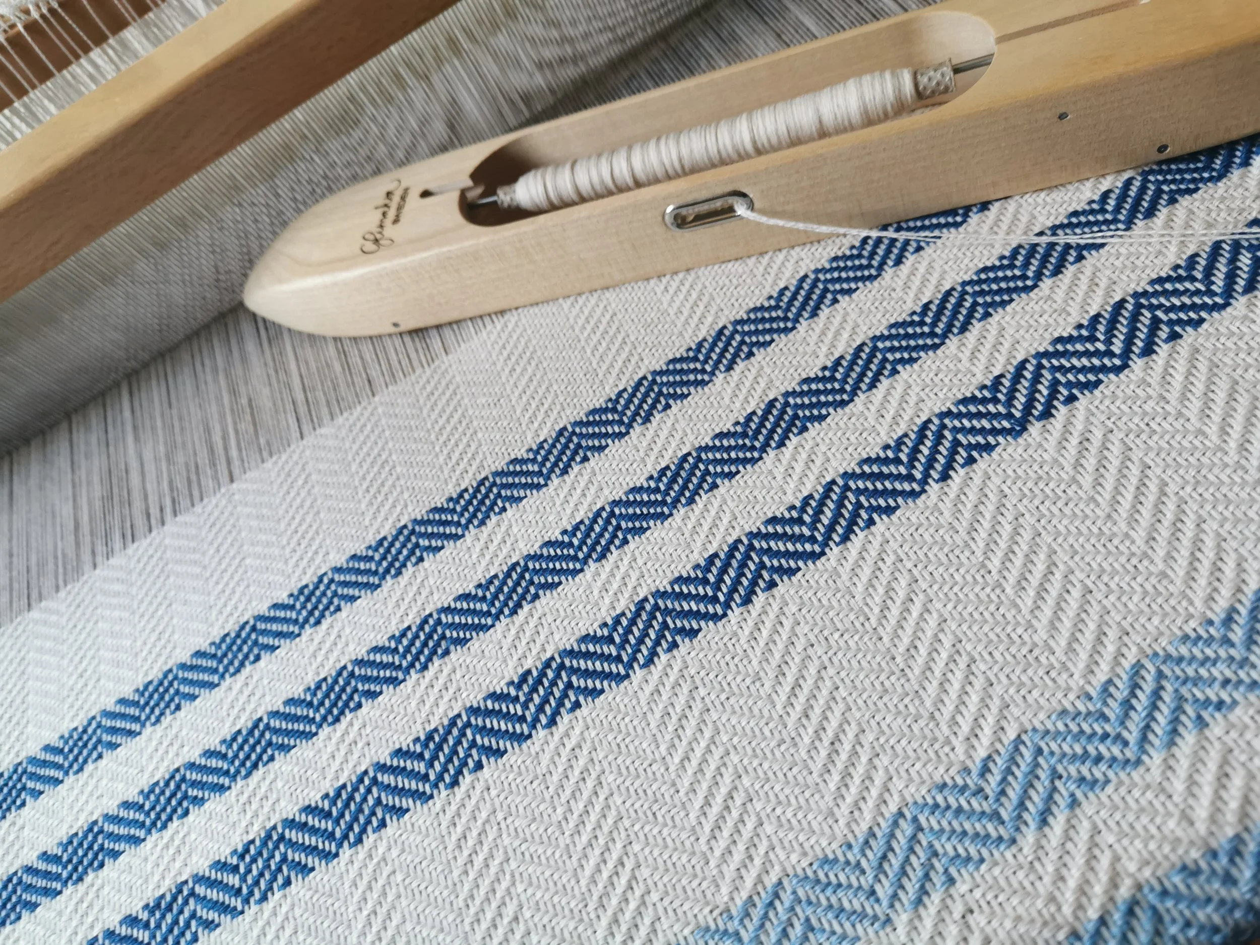 Écharpe Rivage en cours de tissage sur métier à bras, motif chevrons bleu et rayures sur fond blanc