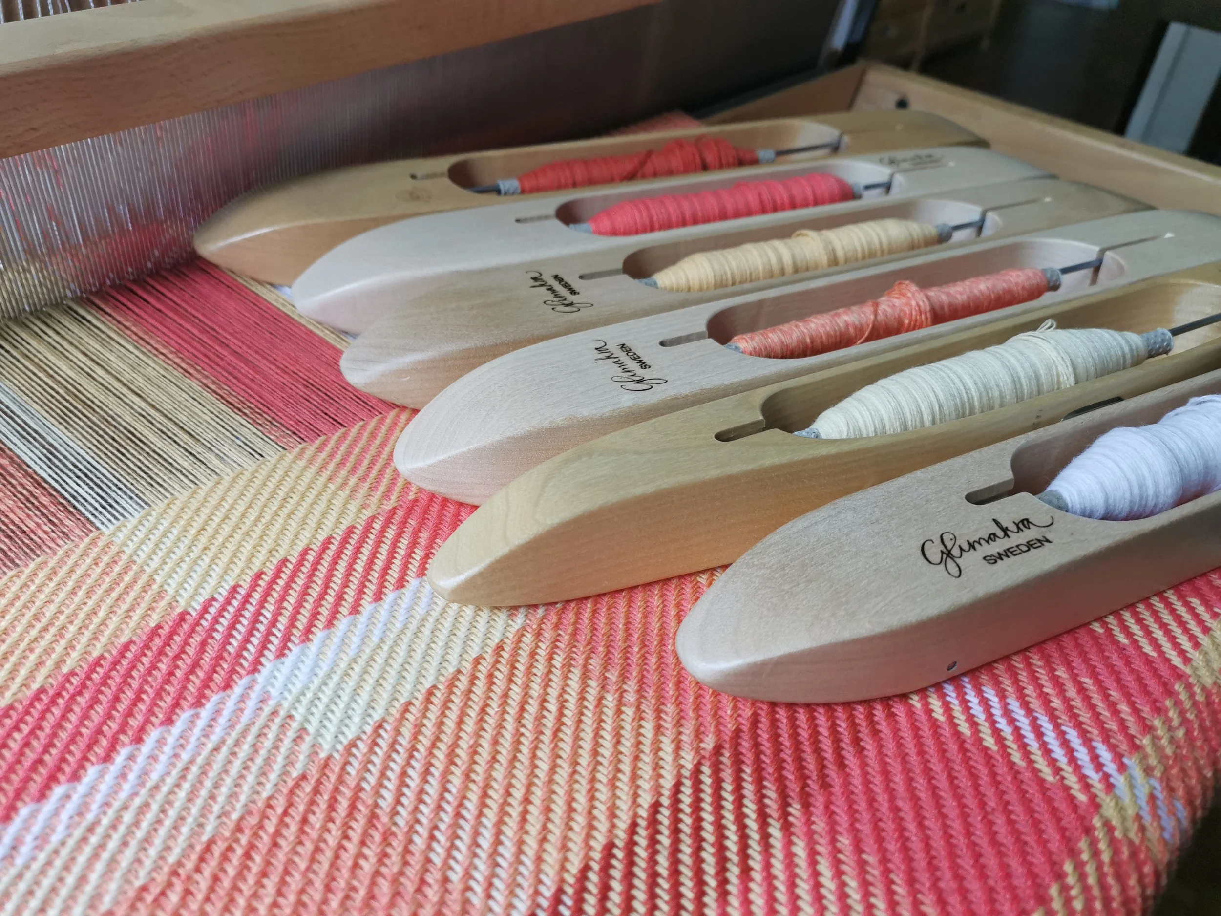 couleurs-metier.jpg	Quatre navettes en bois garnies de fils corail, rouge, jaune et blanc, posées sur le métier à tisser et l'écharpe Mandarine