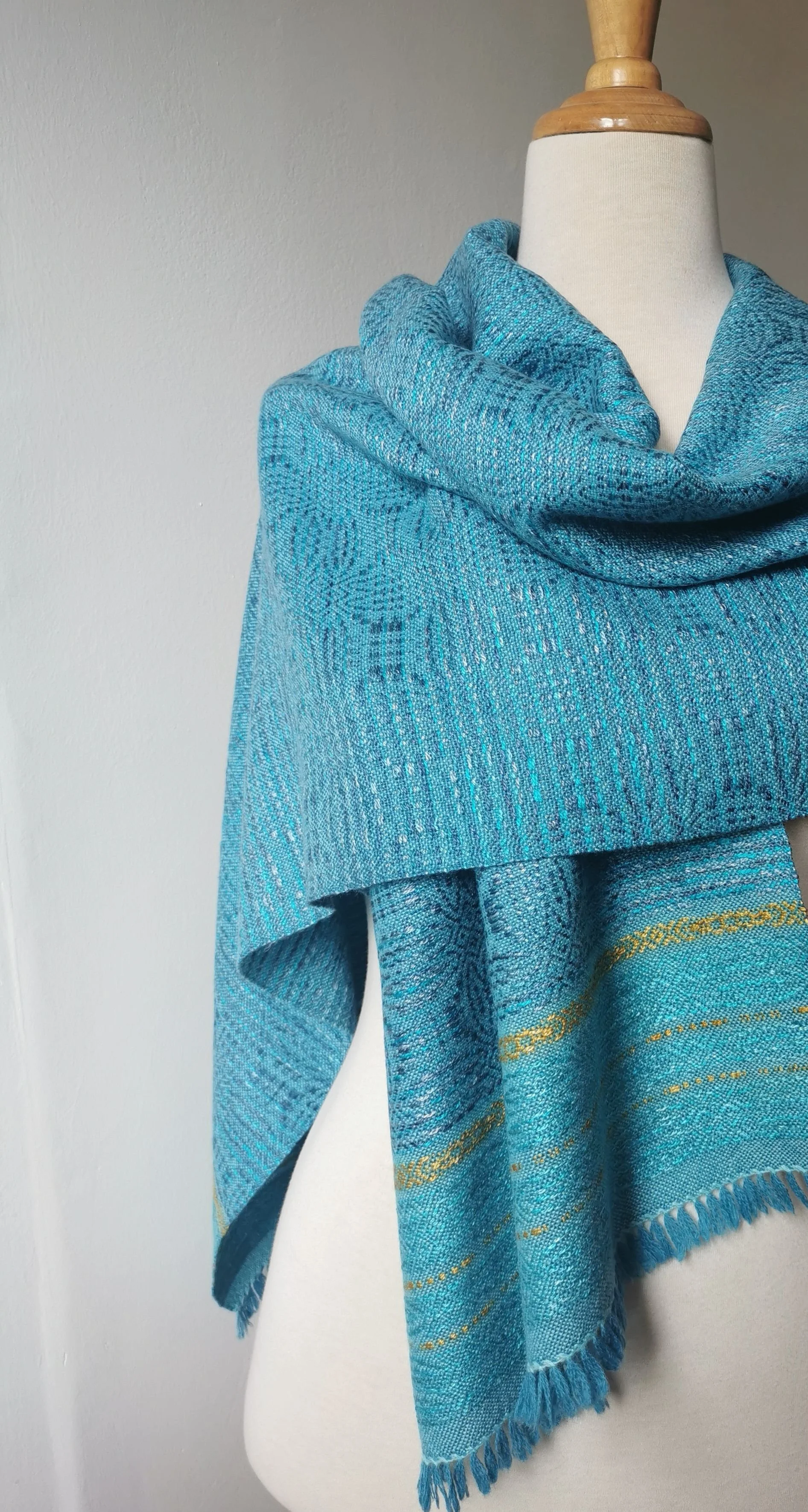 Étole Calypso en cachemire et soie drapée autour du cou d'un mannequin, fond turquoise chiné, motif en relief et bandes dorées