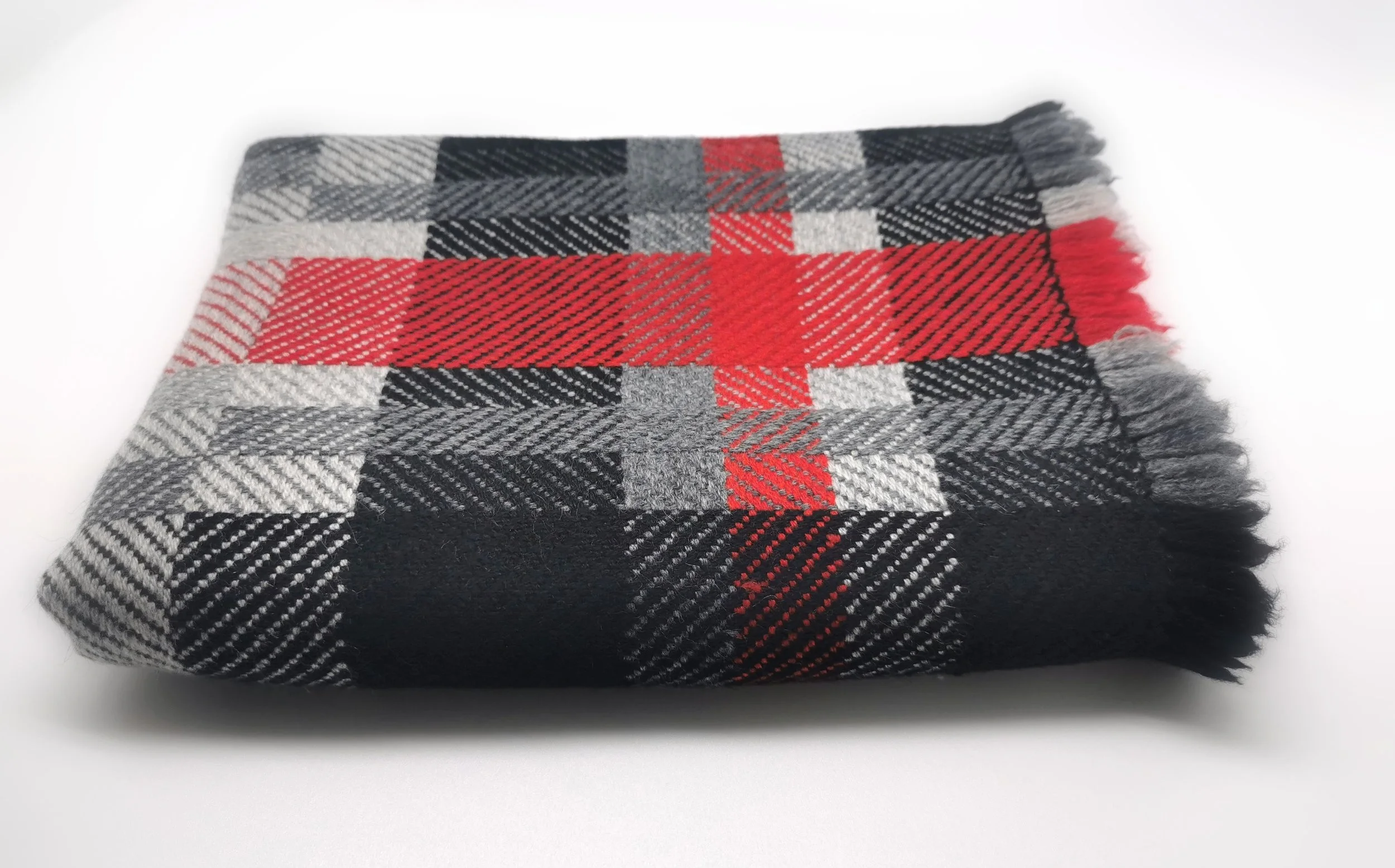 Écharpe Graphite en pur cachemire pliée à plat, motif de carreaux en noir, gris, blanc et rouge vif, franges visibles sur le bord