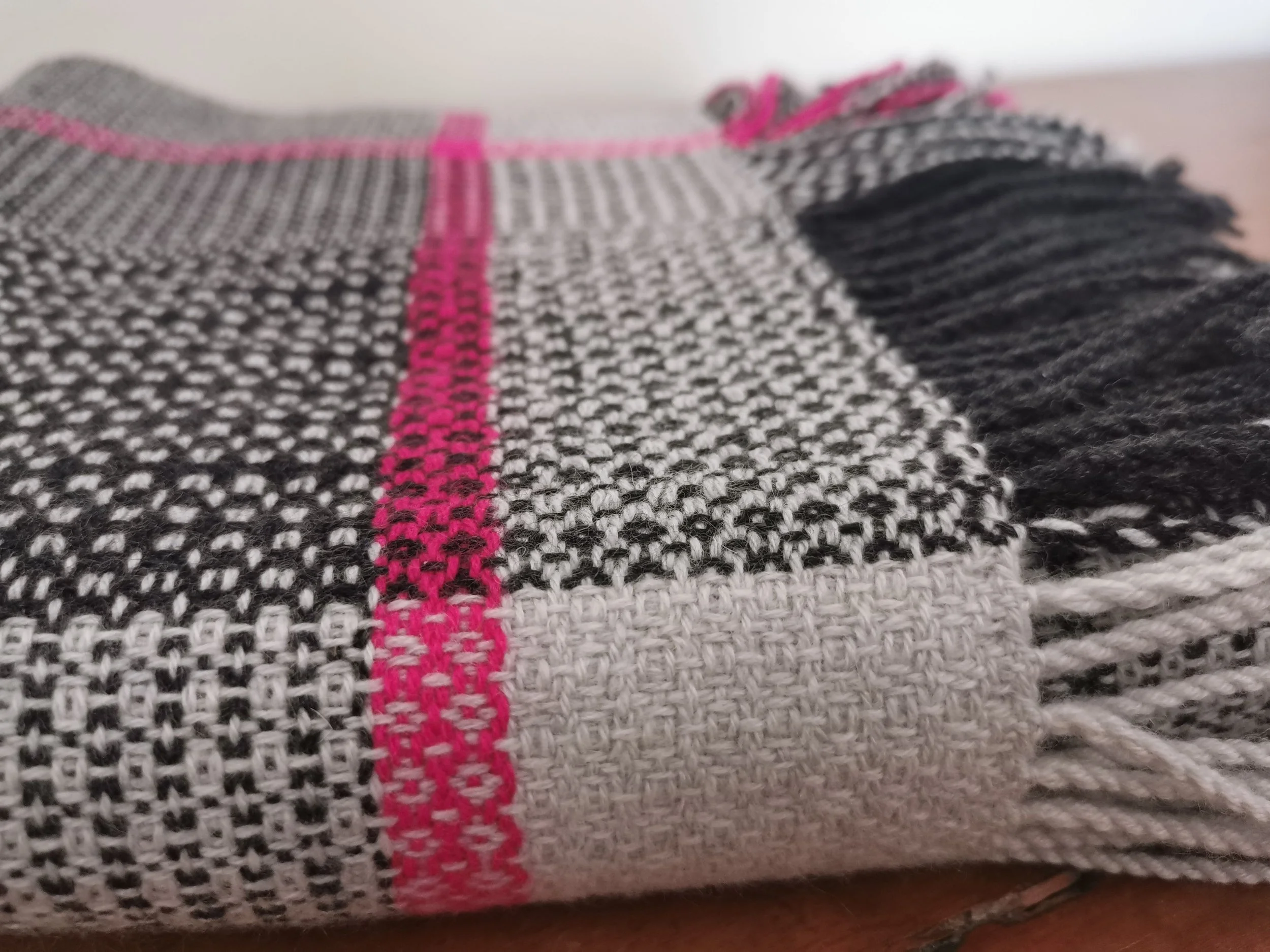 Détail du tissage de l'écharpe Quadrille en pur cachemire, carreaux gris et bande rose fuchsia