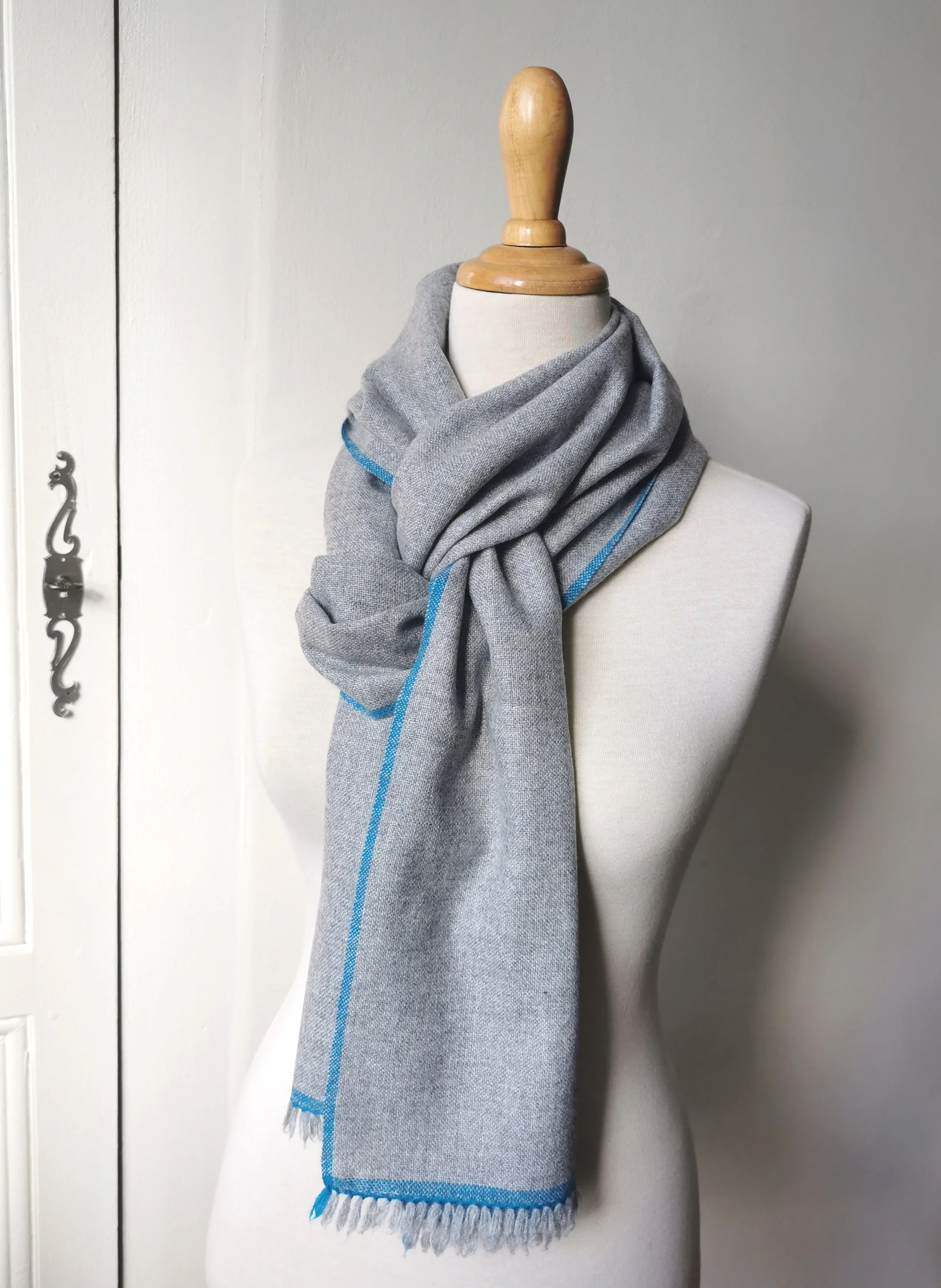 Écharpe Épure en pur cachemire gris chiné nouée autour du cou, fine bande bleu vif, franges libres