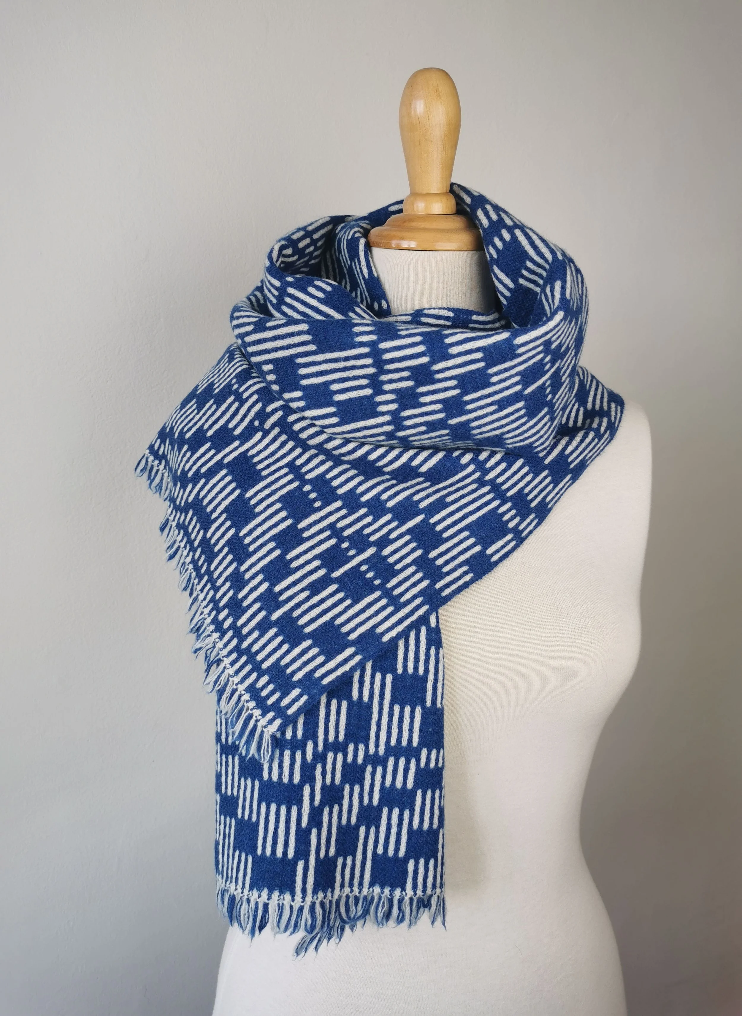 Écharpe Sillage enroulée autour du cou d'un mannequin : face bleu cobalt à tirets écrus, courtes franges libres visibles