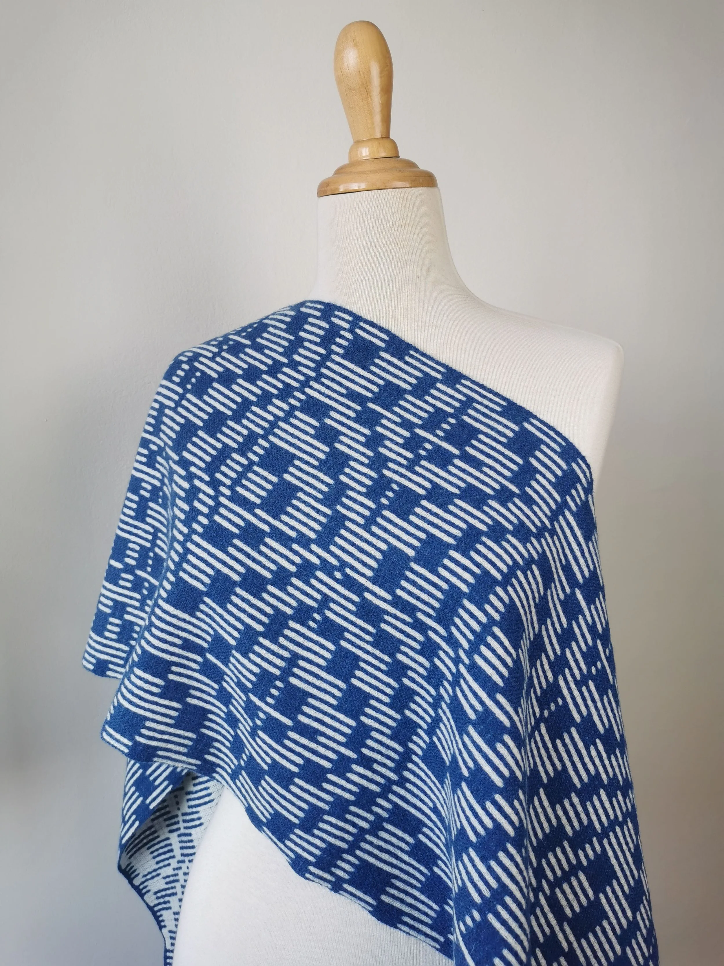 Écharpe Sillage drapée sur l'épaule d'un mannequin : face bleu cobalt à motif de tirets écrus, l'autre face visible au pli