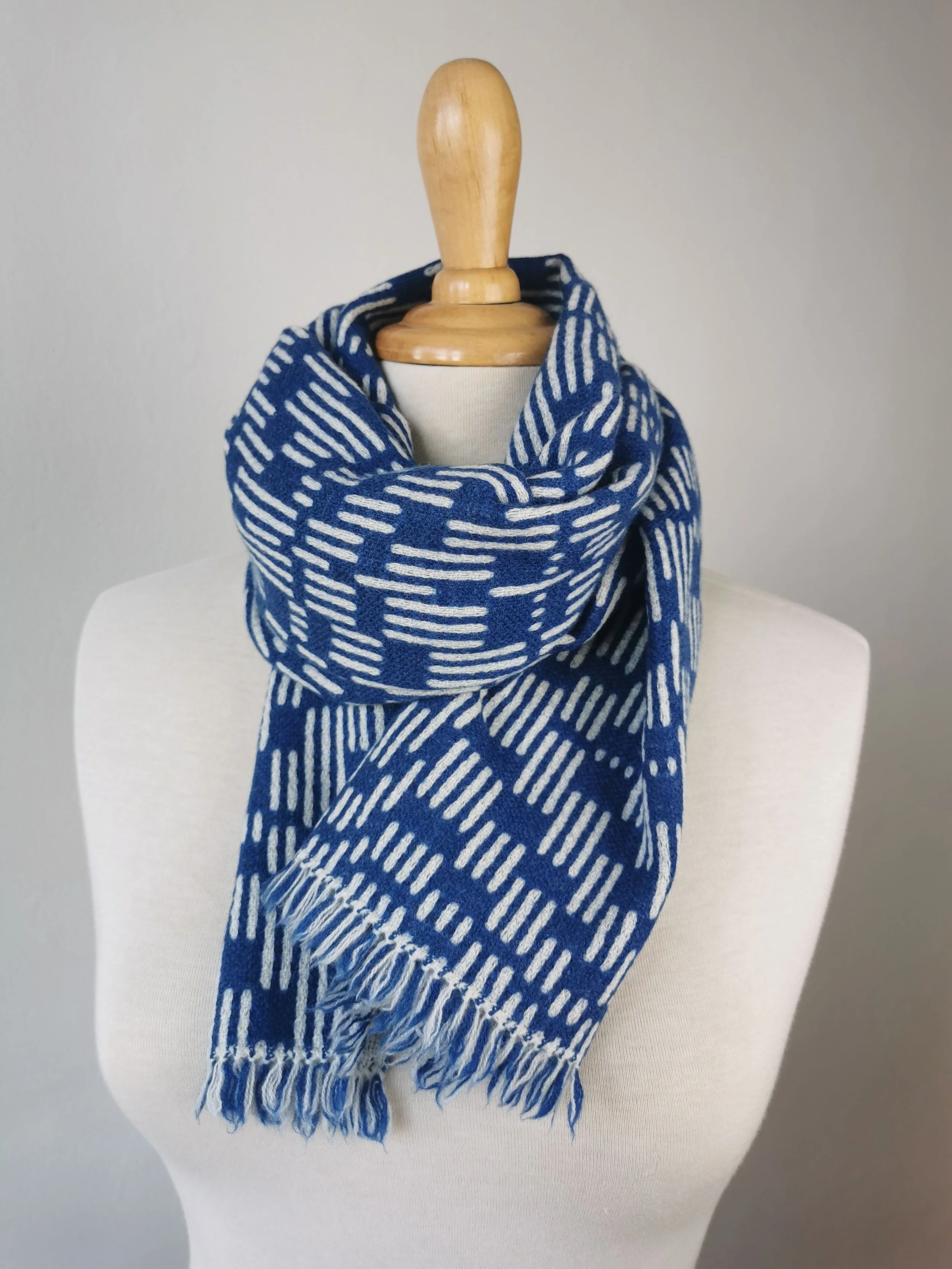 Écharpe Sillage nouée autour du cou d'un mannequin : face bleu cobalt à tirets écrus, courtes franges libres visibles en bas