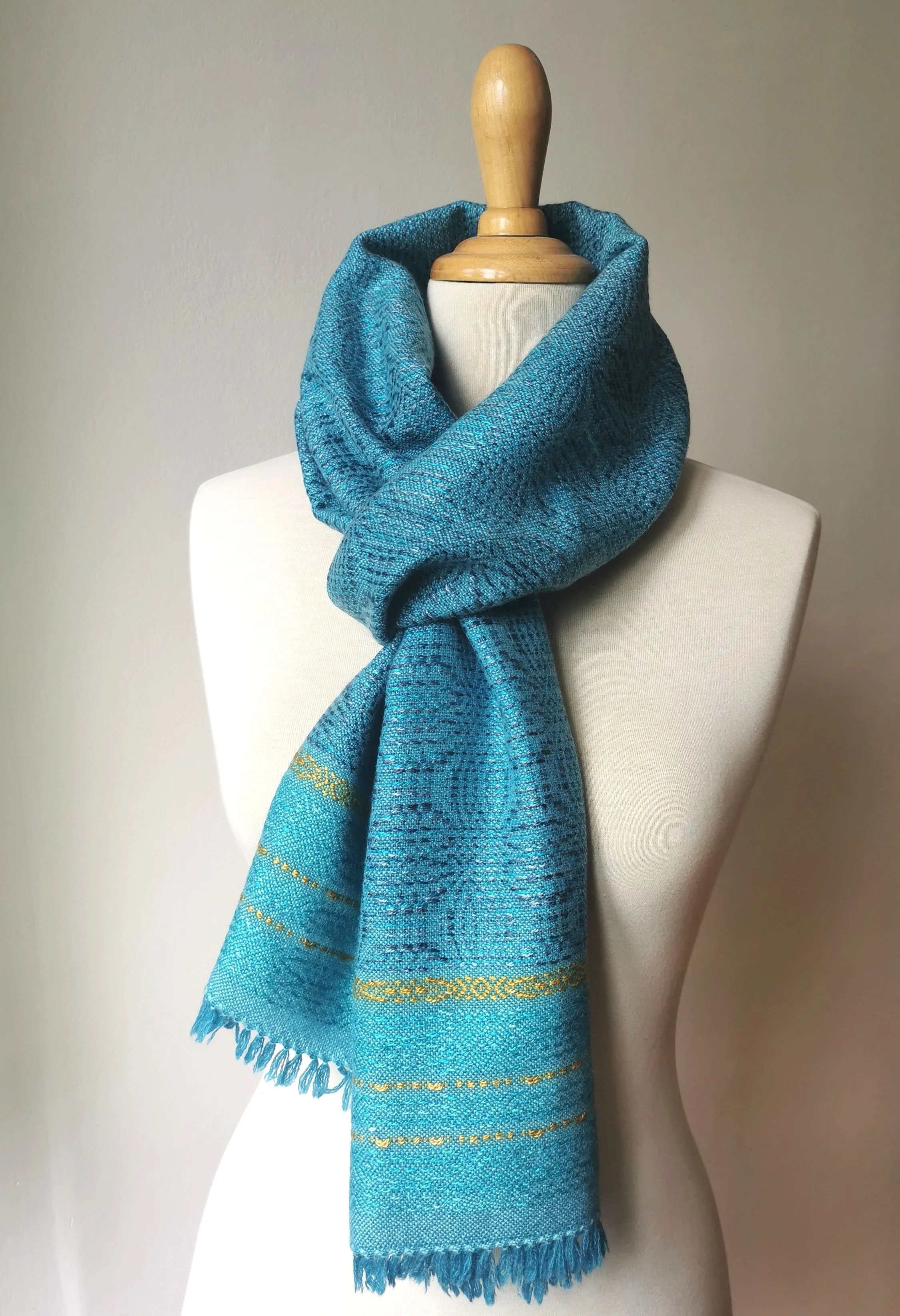 Étole Calypso en cachemire et soie nouée autour du cou d'un mannequin, fond turquoise chiné avec plusieurs bandes de motif doré