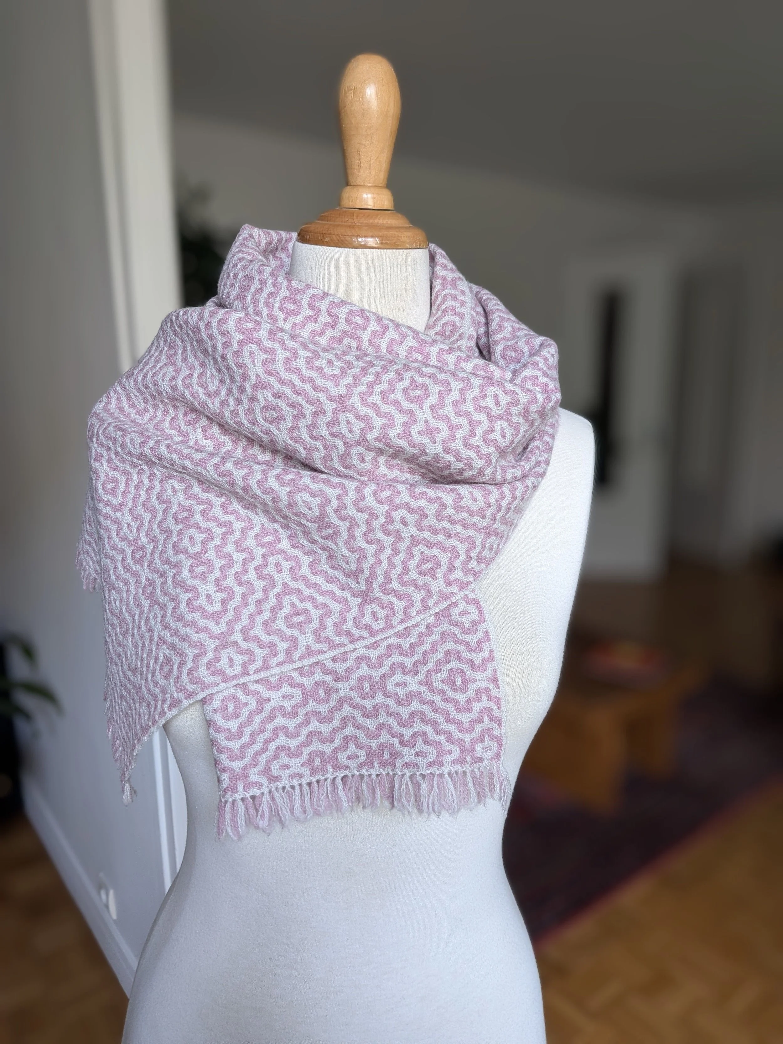 Écharpe Rosée en pur cachemire drapée autour du cou et sur l'épaule d'un mannequin : dessin ondulé rose poudré sur fond ivoire