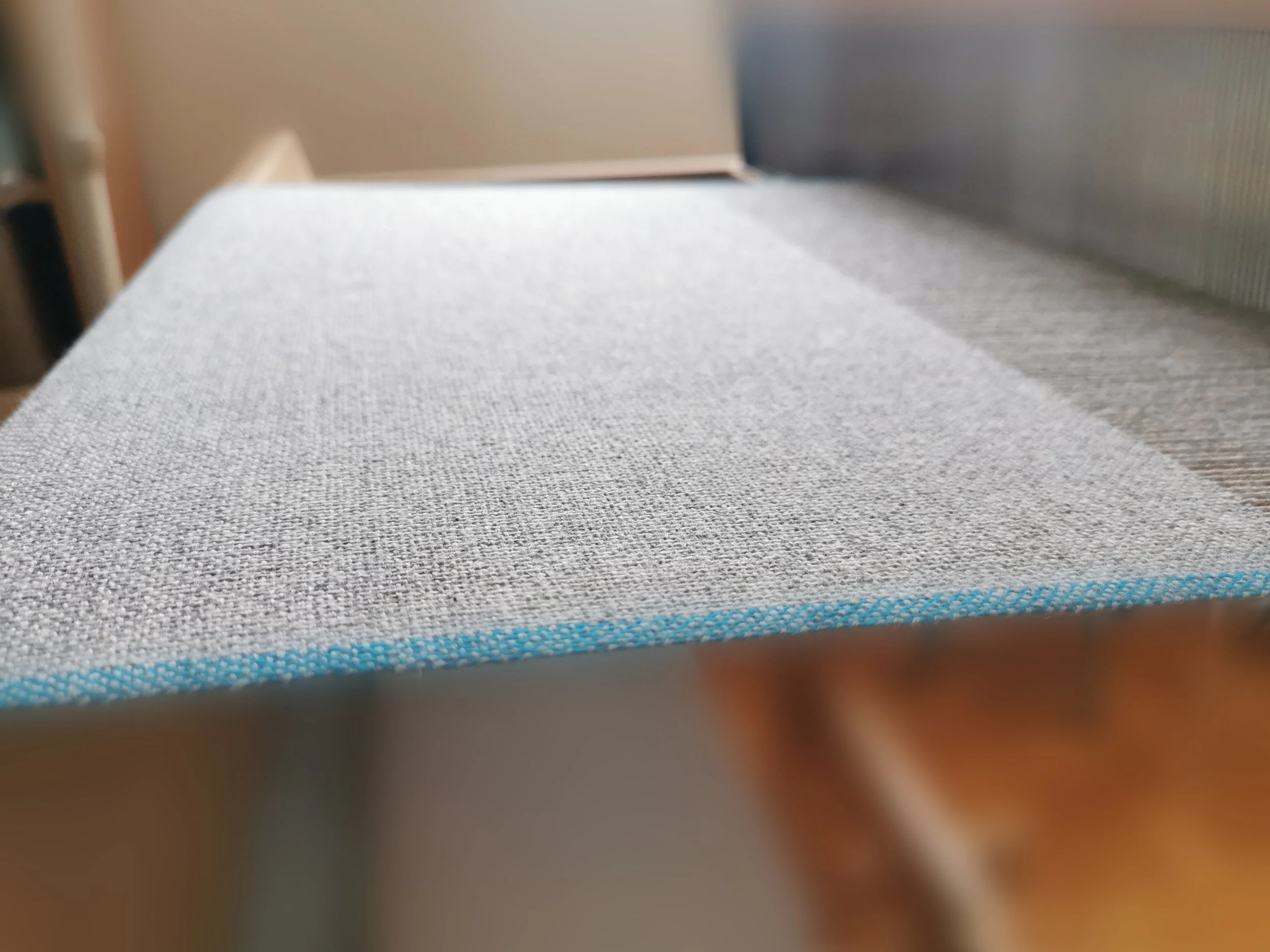 Écharpe Épure en cours de tissage sur métier à bras, gros plan sur l'armure toile en cachemire gris chiné et la lisière bleu vif