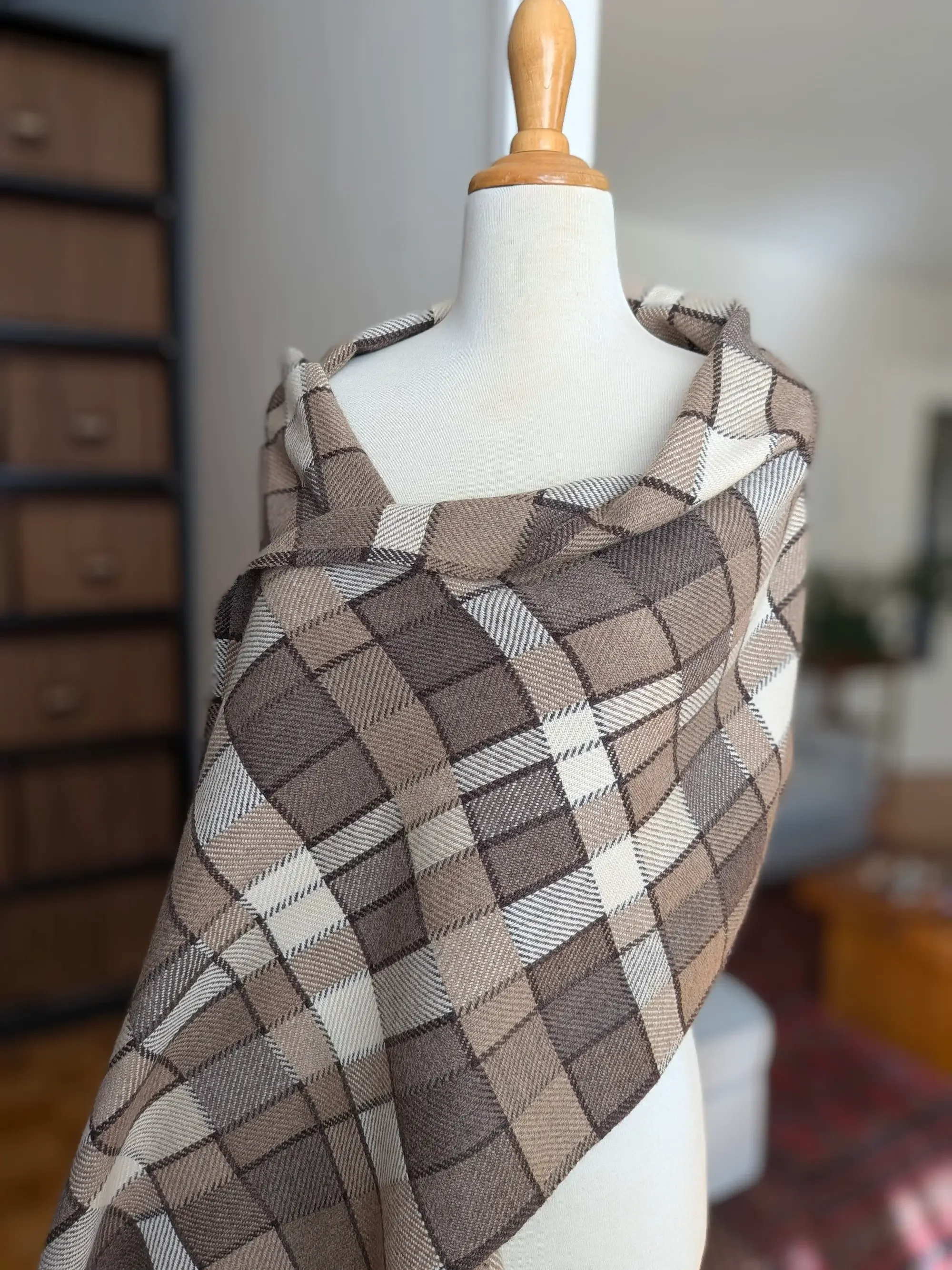 Écharpe Agate en cachemire portée sur les épaules d’un mannequin, vue rapprochée des carreaux taupe, brun foncé et blanc cassé aux fines diagonales