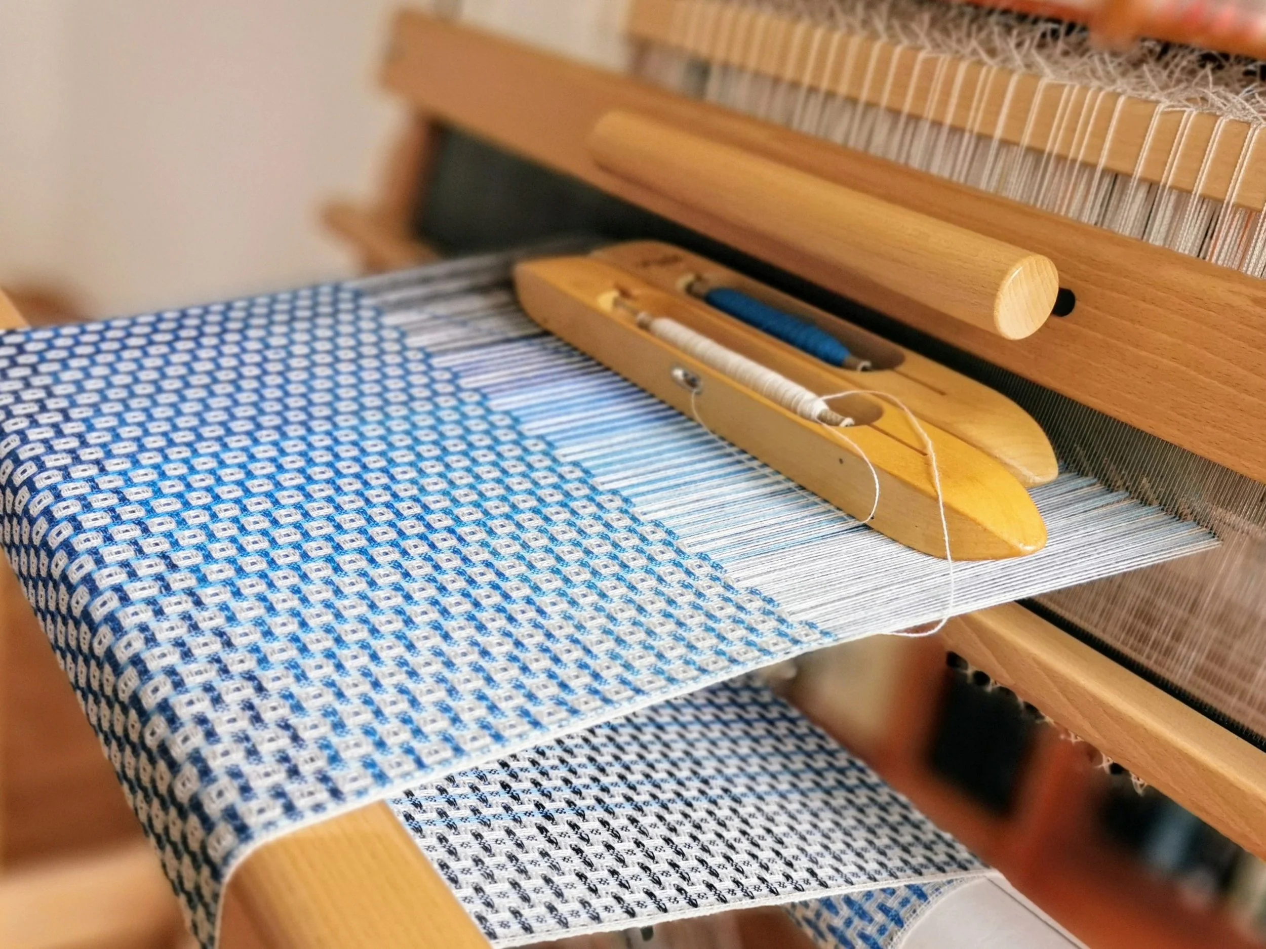 Vue d'un métier à tisser avec une écharpe en cachemire à motifs bleus et blancs en cours de fabrication.