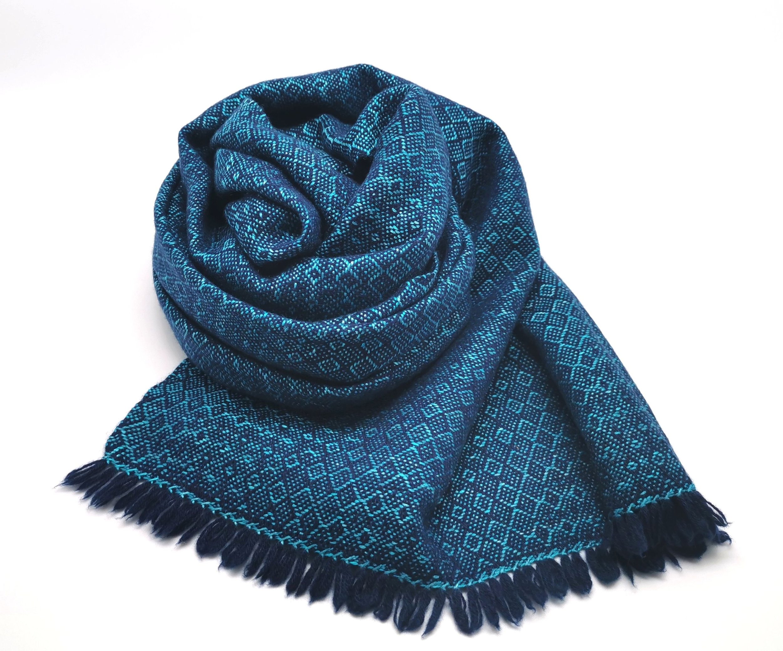 Étole Ondine en cachemire et soie roulée sur elle-même, motif en losanges dans un camaïeu de bleu marine et turquoise, franges visibles