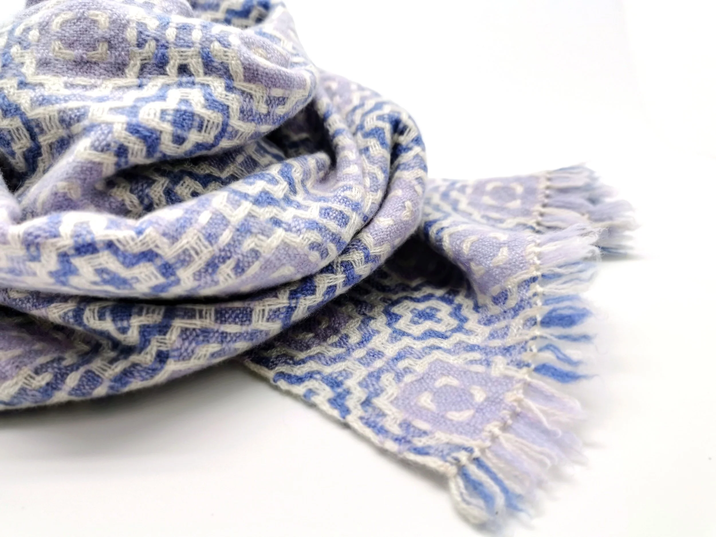 Gros plan sur l'écharpe Lilas en pur cachemire : motif géométrique en viloet foncé et violet pâle sur fond blanc, courtes franges libres