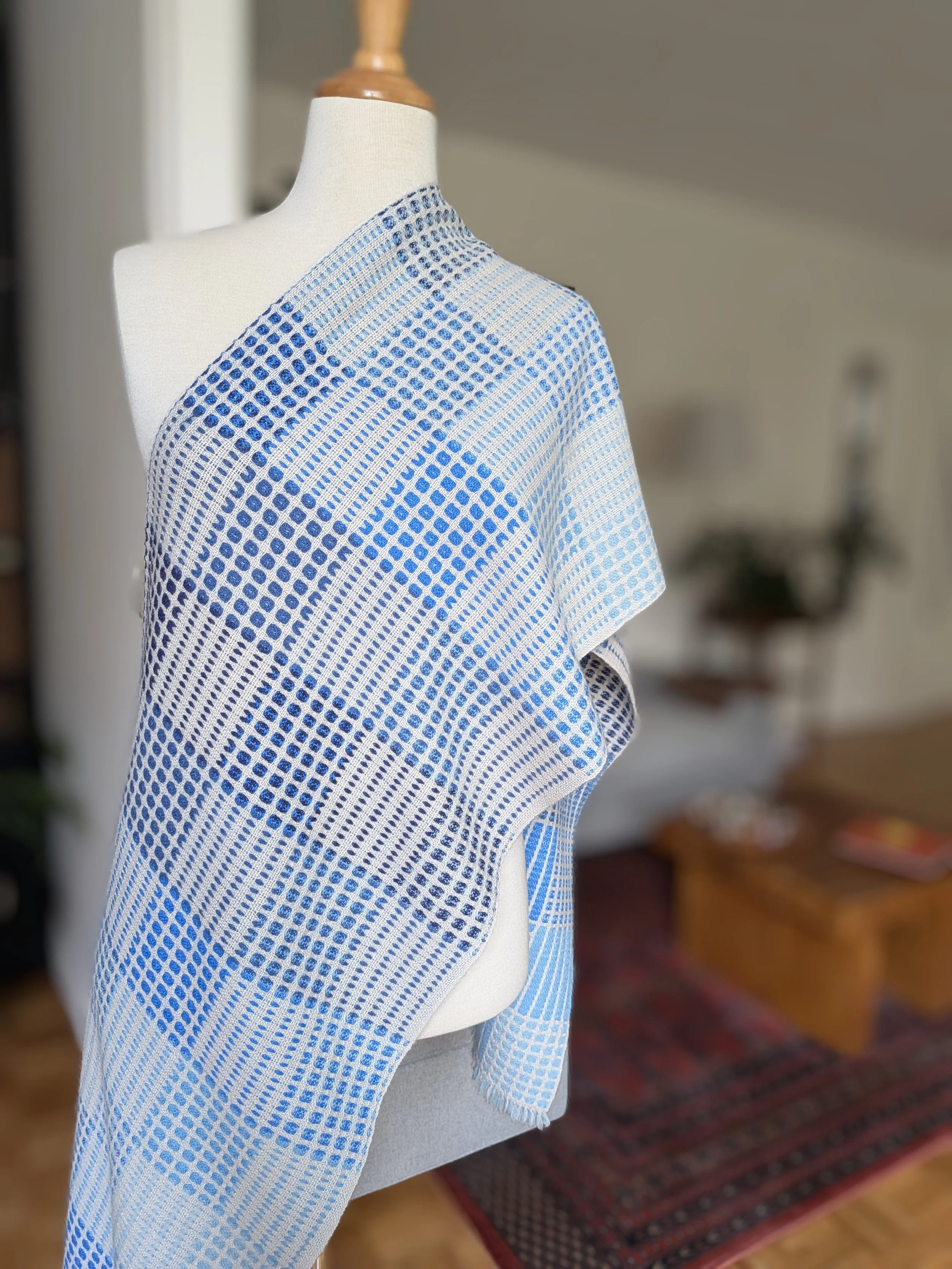 Écharpe Variation en bleu drapée en diagonale sur l'épaule d'un mannequin, face claire à dominante écrue : pois bleus du marine au bleu clair répartis en zones