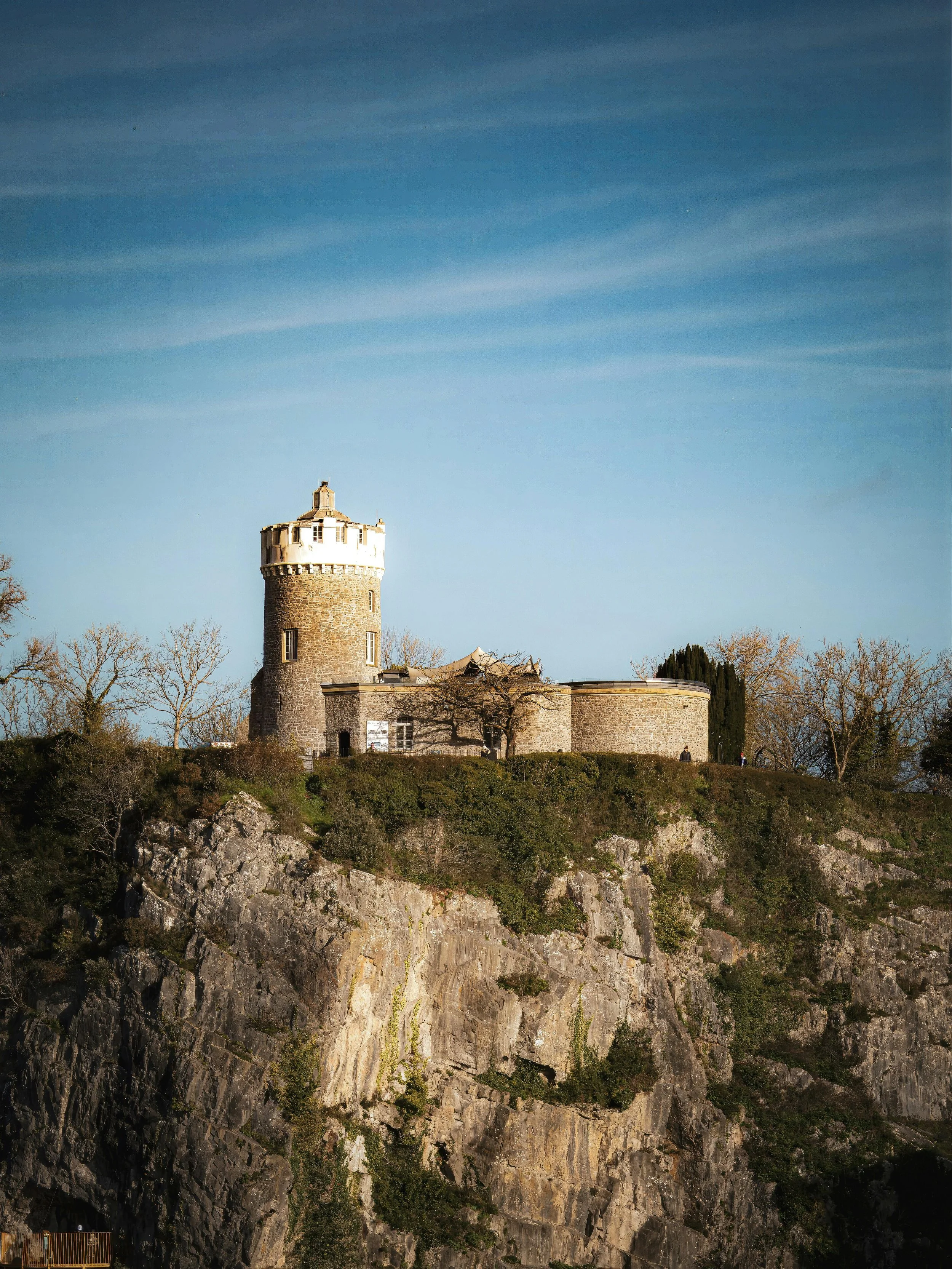A castle-like stone tower on a hilltop with a clear sky in the background.