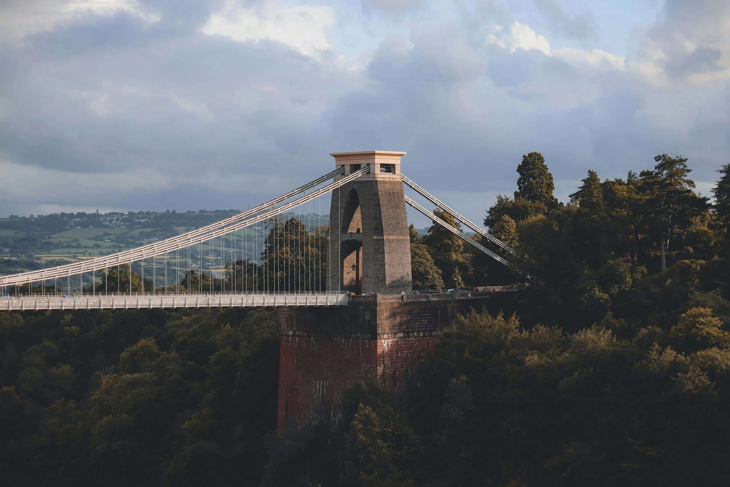 The Clifton Suspension Bridge spanning a lush green valley with a cloudy sky overhead.
