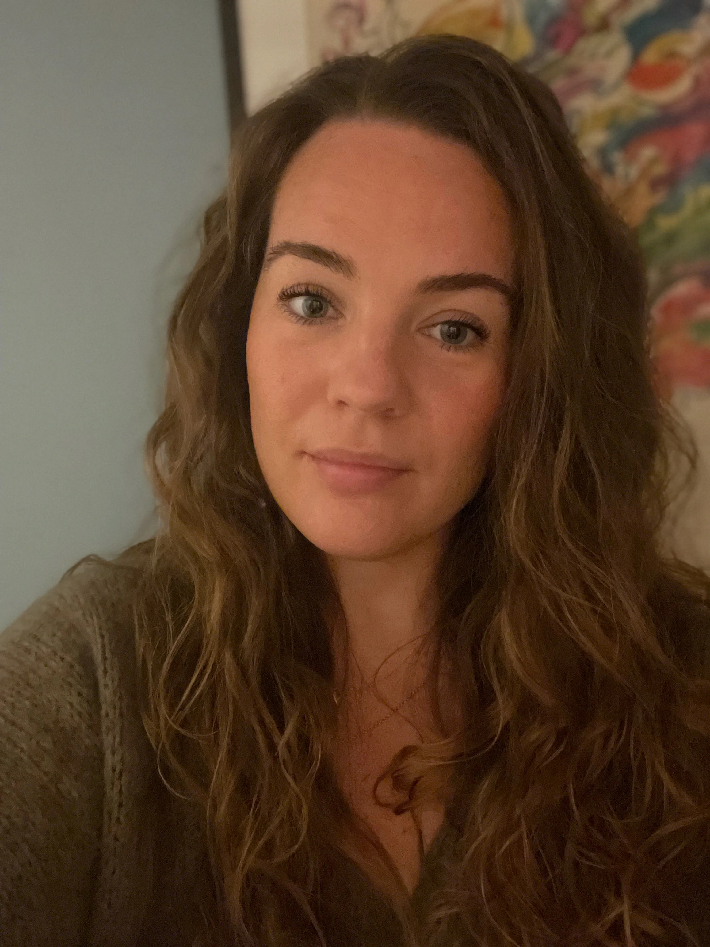 Close-up of a woman with wavy brown hair and blue eyes, smiling softly.