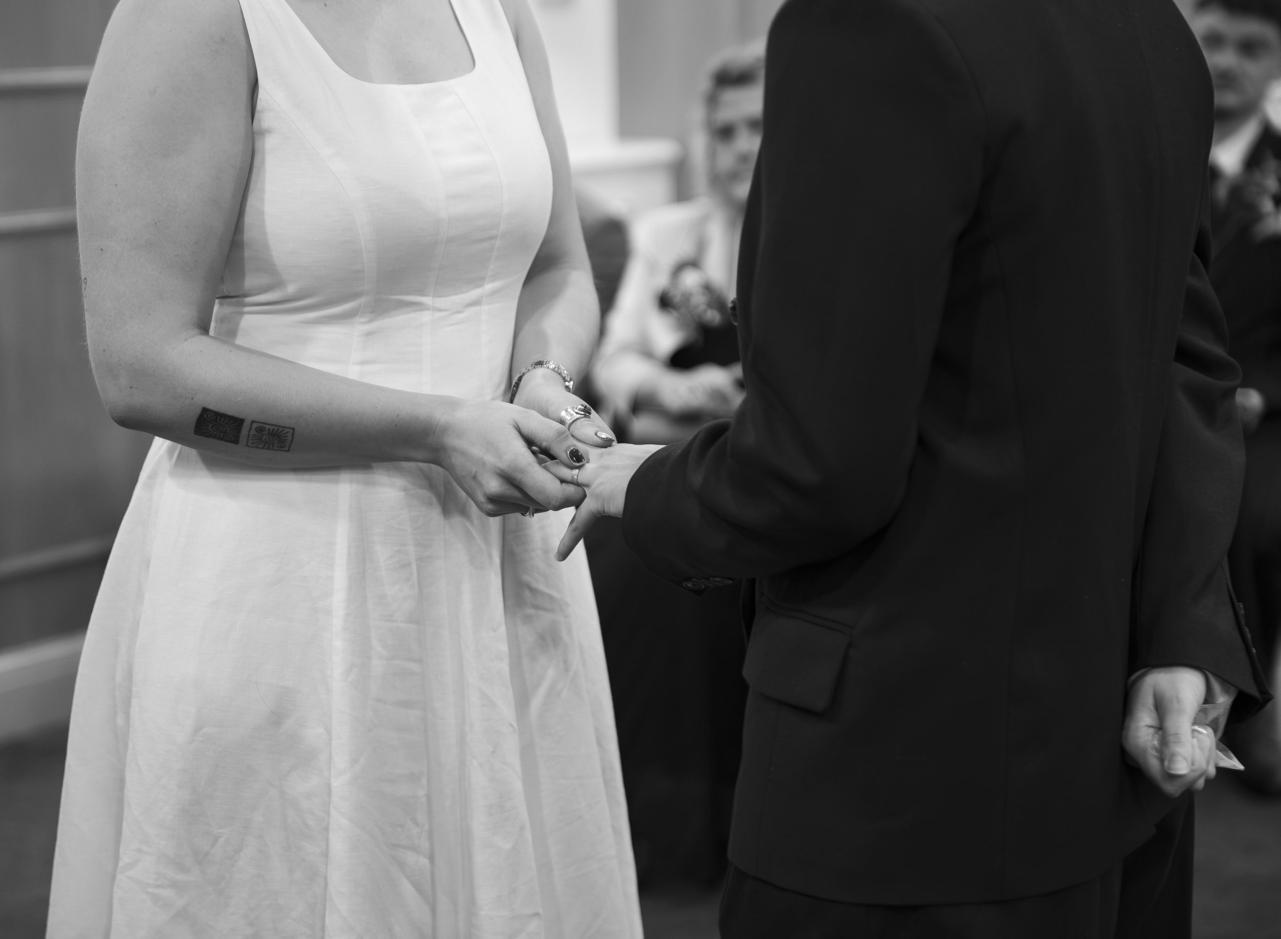 A person wearing a black suit holding hands with a person dressed in a white gown, in a close-up shot.