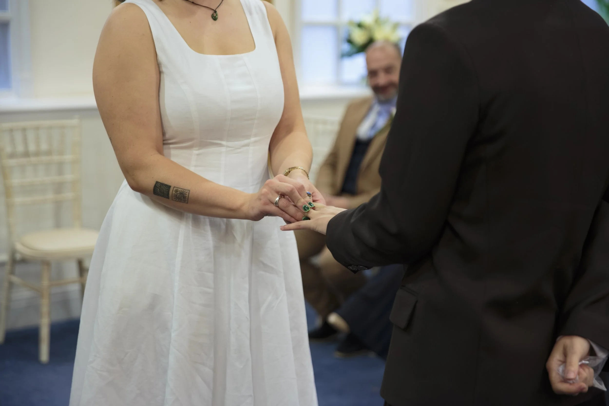A woman in a white dress holding hands with a man in a black suit during a wedding ceremony, with another man in the background.
