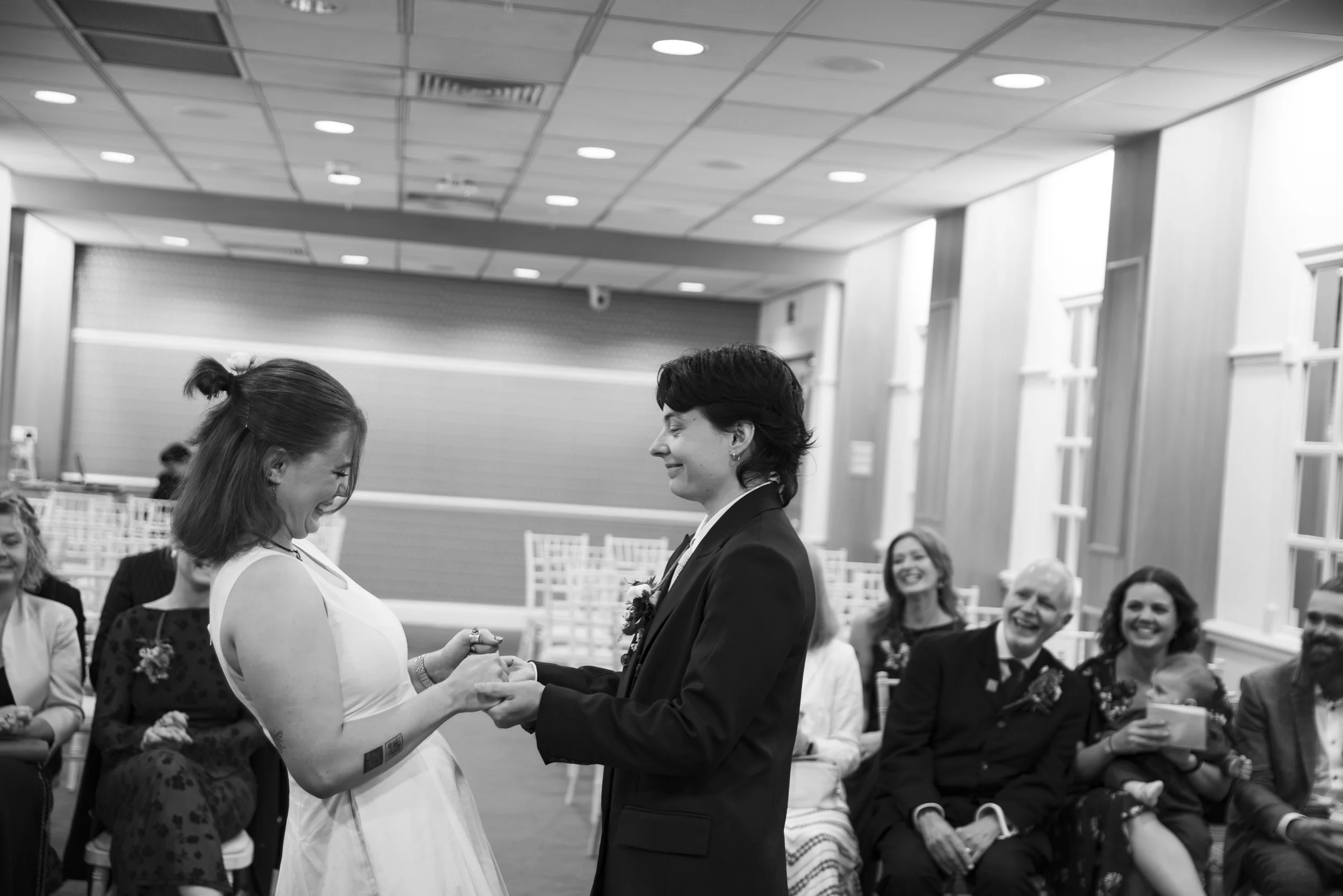 A couple gets married in a ceremony with guests seated around, exchanging vows and looking happy.