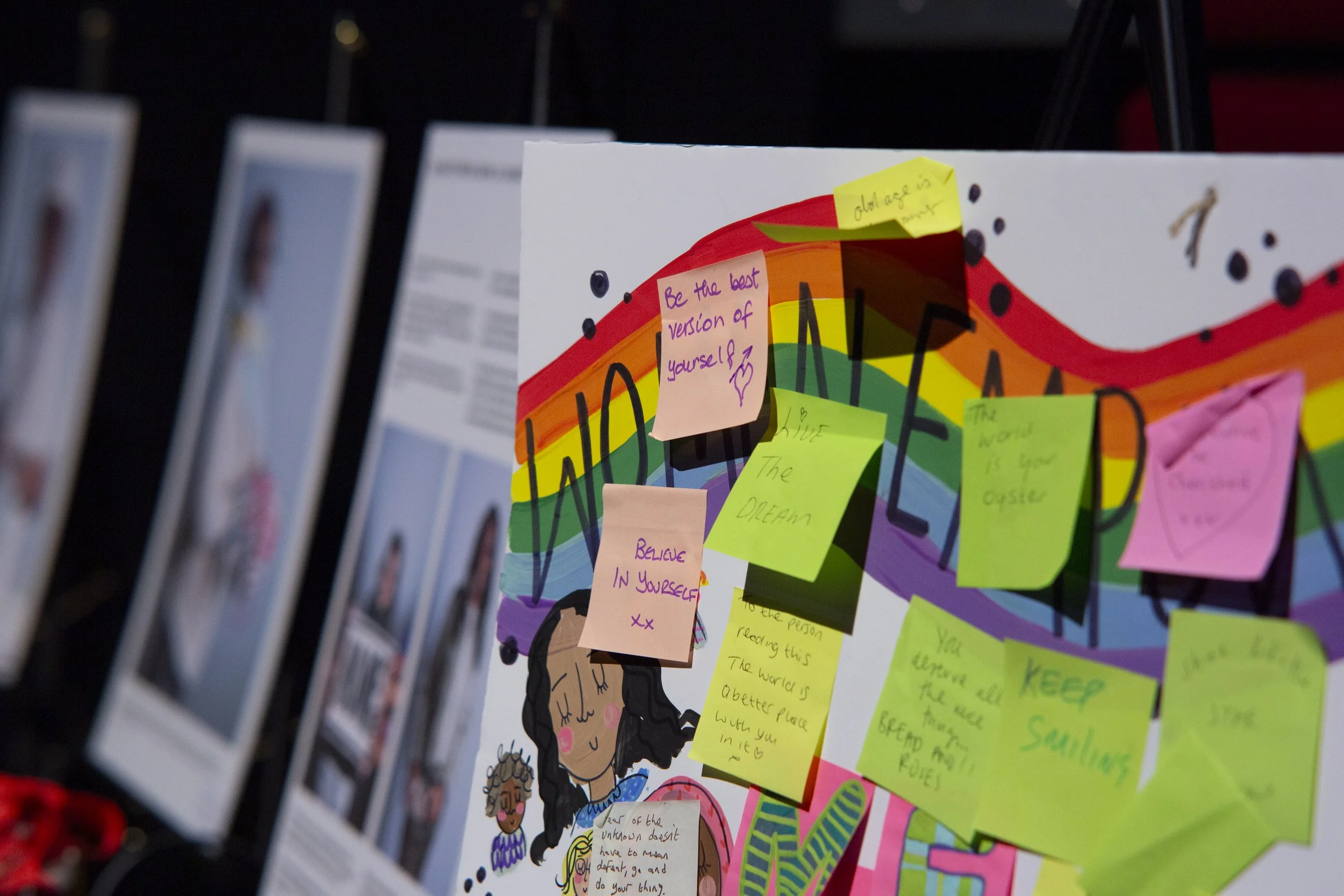 Close-up of a colorful bulletin board with various inspirational notes, including one that says 'Be the best version of yourself.' The board features rainbow colors and cartoon illustrations, with sticky notes attached.
