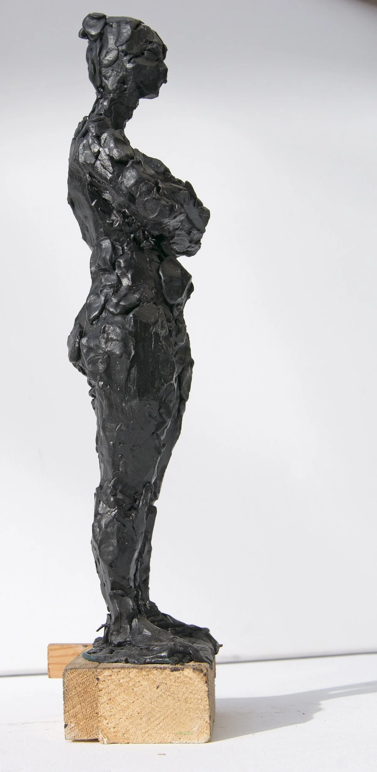 Eine schwarze, abstrakte Skulptur einer aufrecht stehenden menschlichen Figur auf einem Holzsockel.
