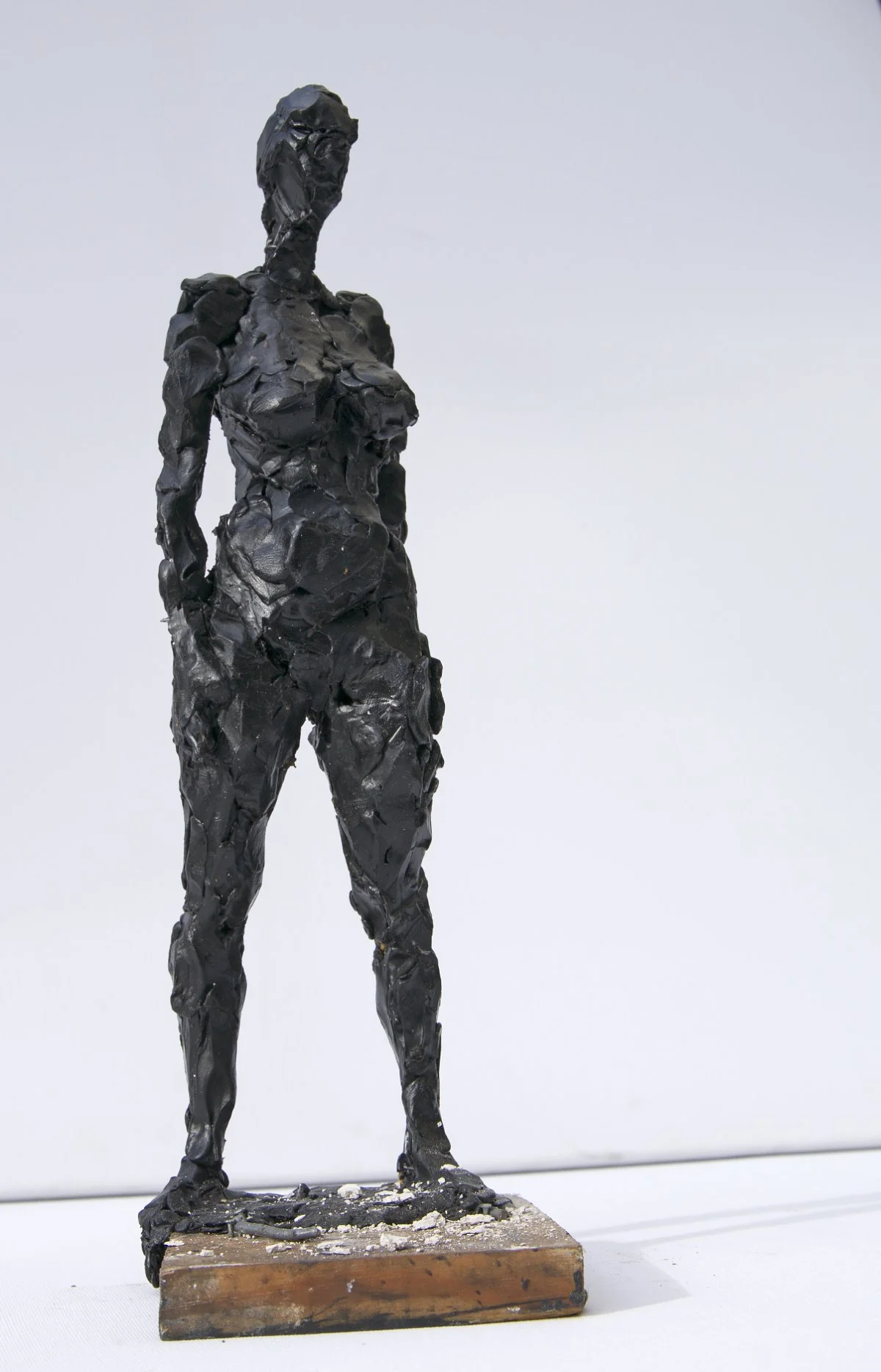 Eine schwarze Skulptur einer stehenden weiblichen Figur mit strukturierter, abstrakter Oberfläche, platziert auf einem Holzsockel.
