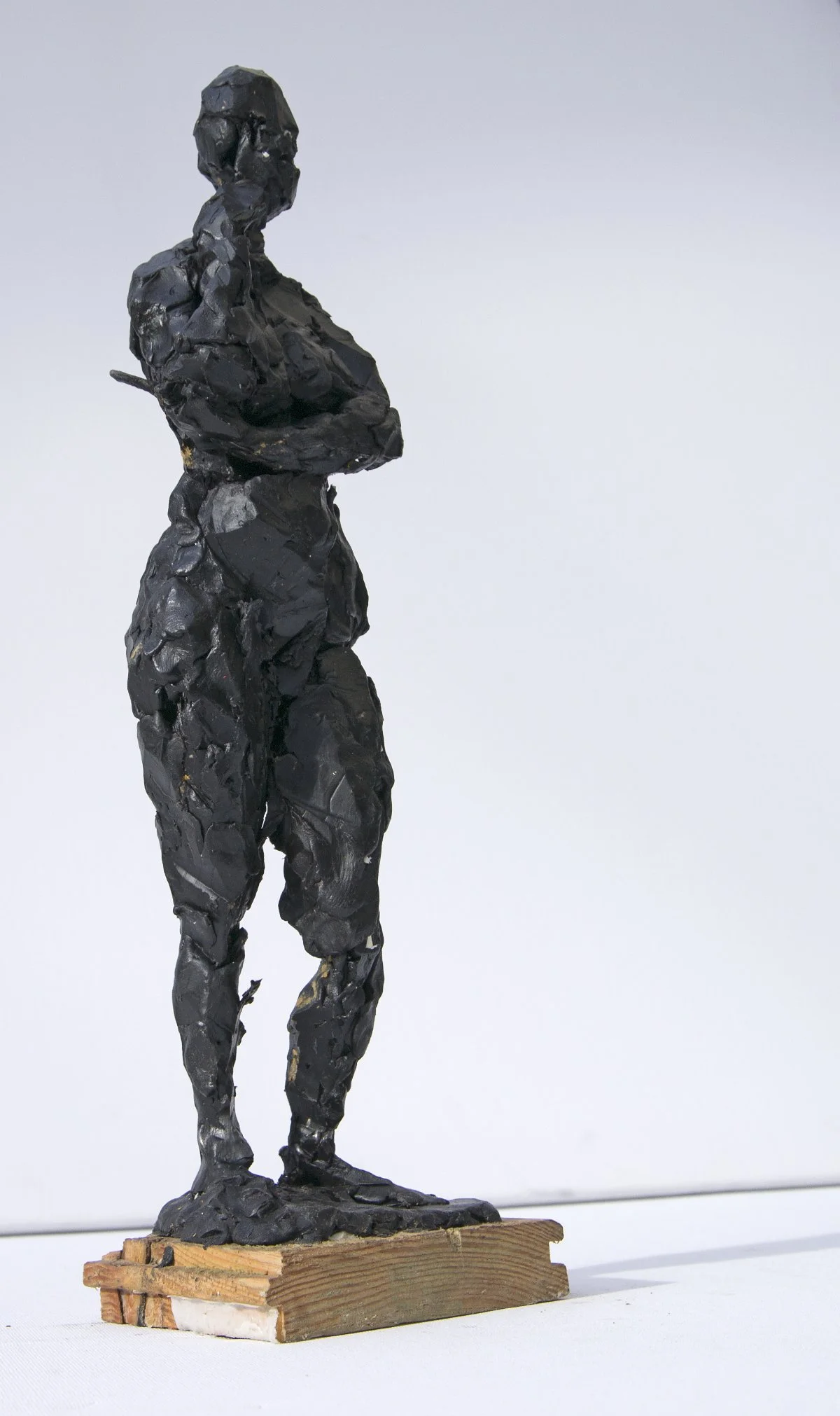 Skulptur einer Frau mit kurzem Haar, die mit verschränkten Armen steht, auf einem Holzsockel montiert.
