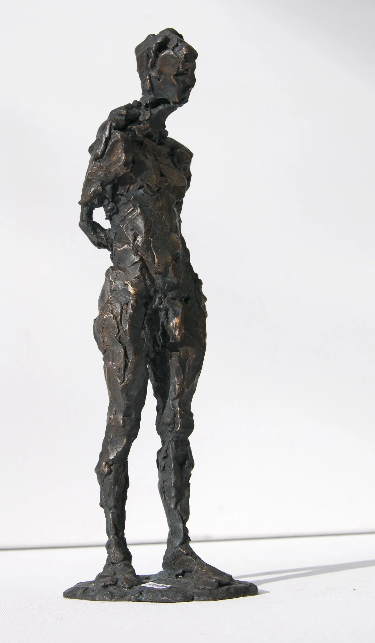 Eine Figurenskulptur einer Frau, die mit in die Hüften gestemmten Händen vor einem weißen Hintergrund steht.
