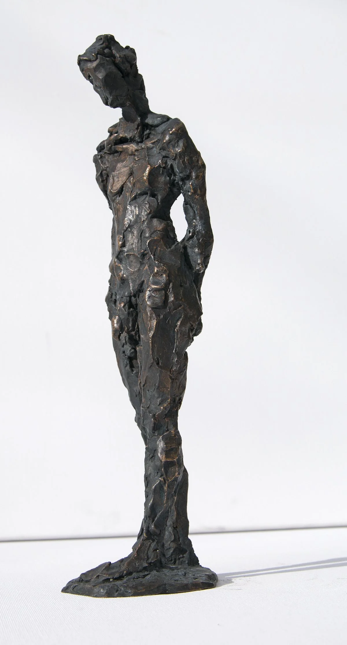 Eine Skulptur einer stehenden Frau mit in die Hüften gestemmten Händen, in einem abstrakten, strukturierten Stil.
