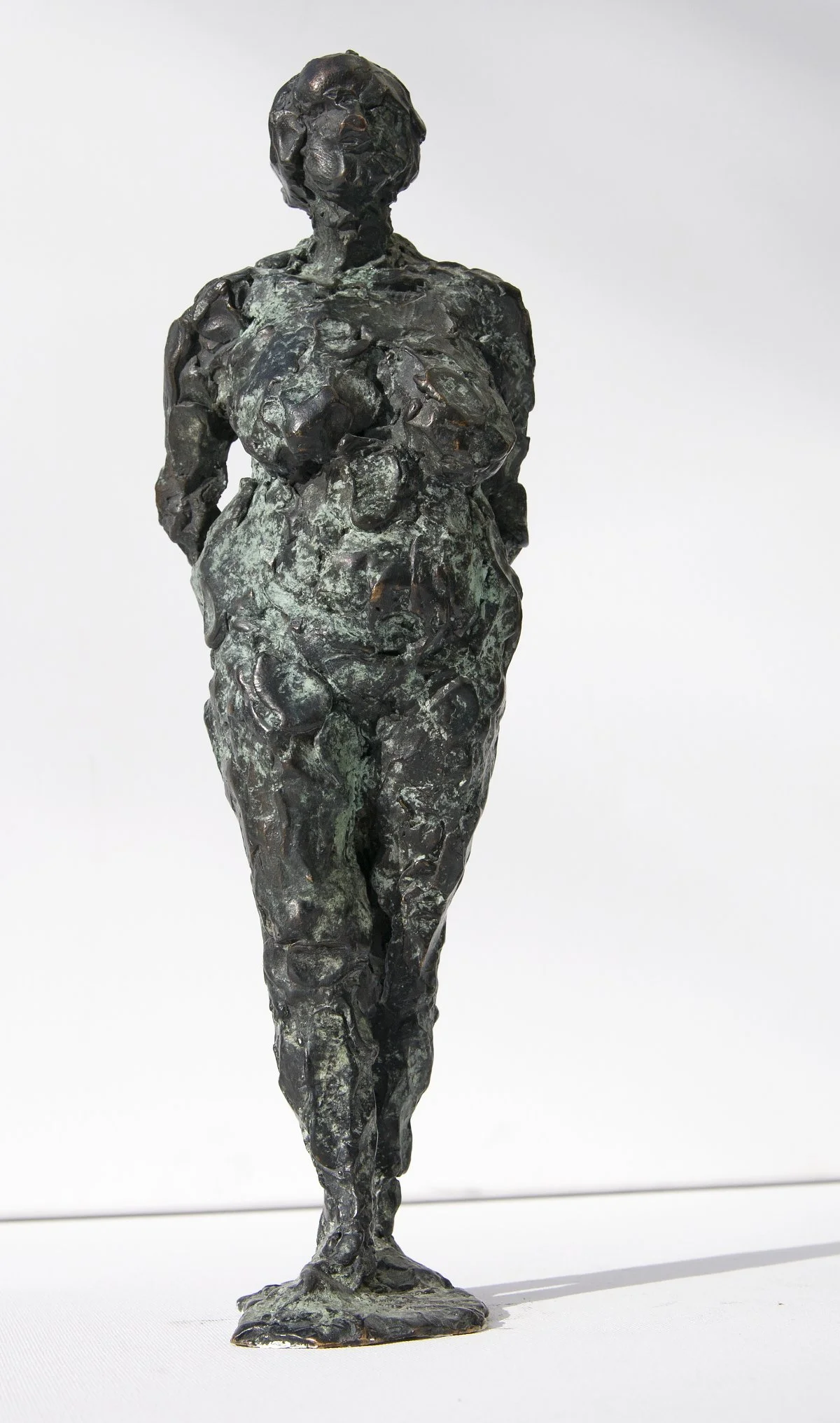 Skulptur einer schwangeren Frau mit abstrakter, strukturierter Oberfläche, die mit hinter dem Rücken verschränkten Händen vor einem schlichten weißen Hintergrund steht.
