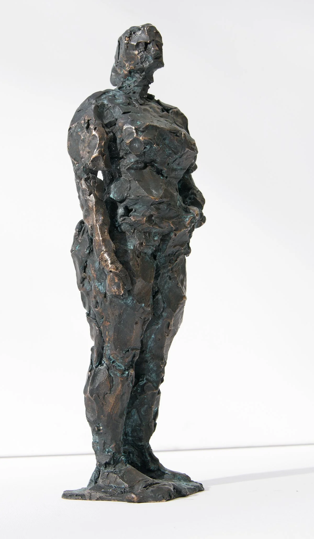 Eine Skulptur einer Frau mit strukturierter, rauer Oberfläche und vereinfachtem Gesichtsausdruck, die eine stehende weibliche Figur vor einem schlichten weißen Hintergrund darstellt.
