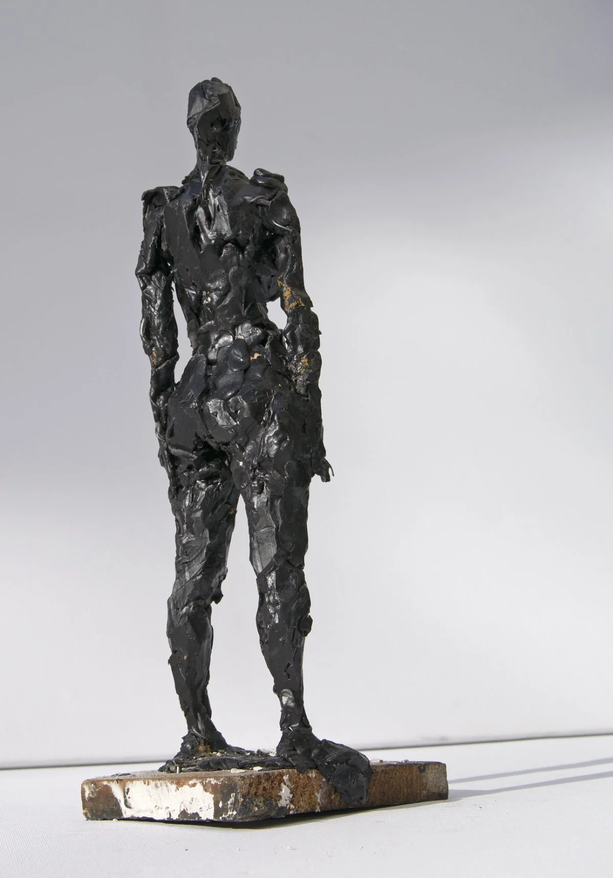 Eine schwarze, strukturierte Skulptur einer stehenden Frau auf einem rechteckigen Sockel.
