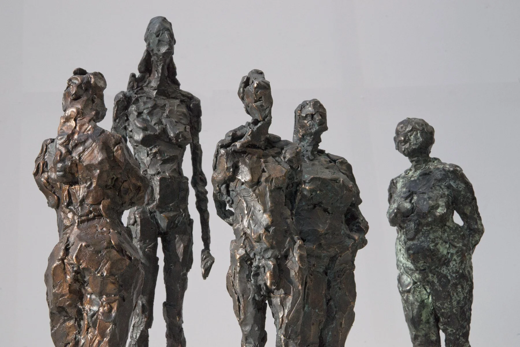 Eine Bronzeskulptur von fünf Personen, jede mit einer rauen, strukturierten Oberfläche, die vor einem schlichten Hintergrund zusammenstehen.
