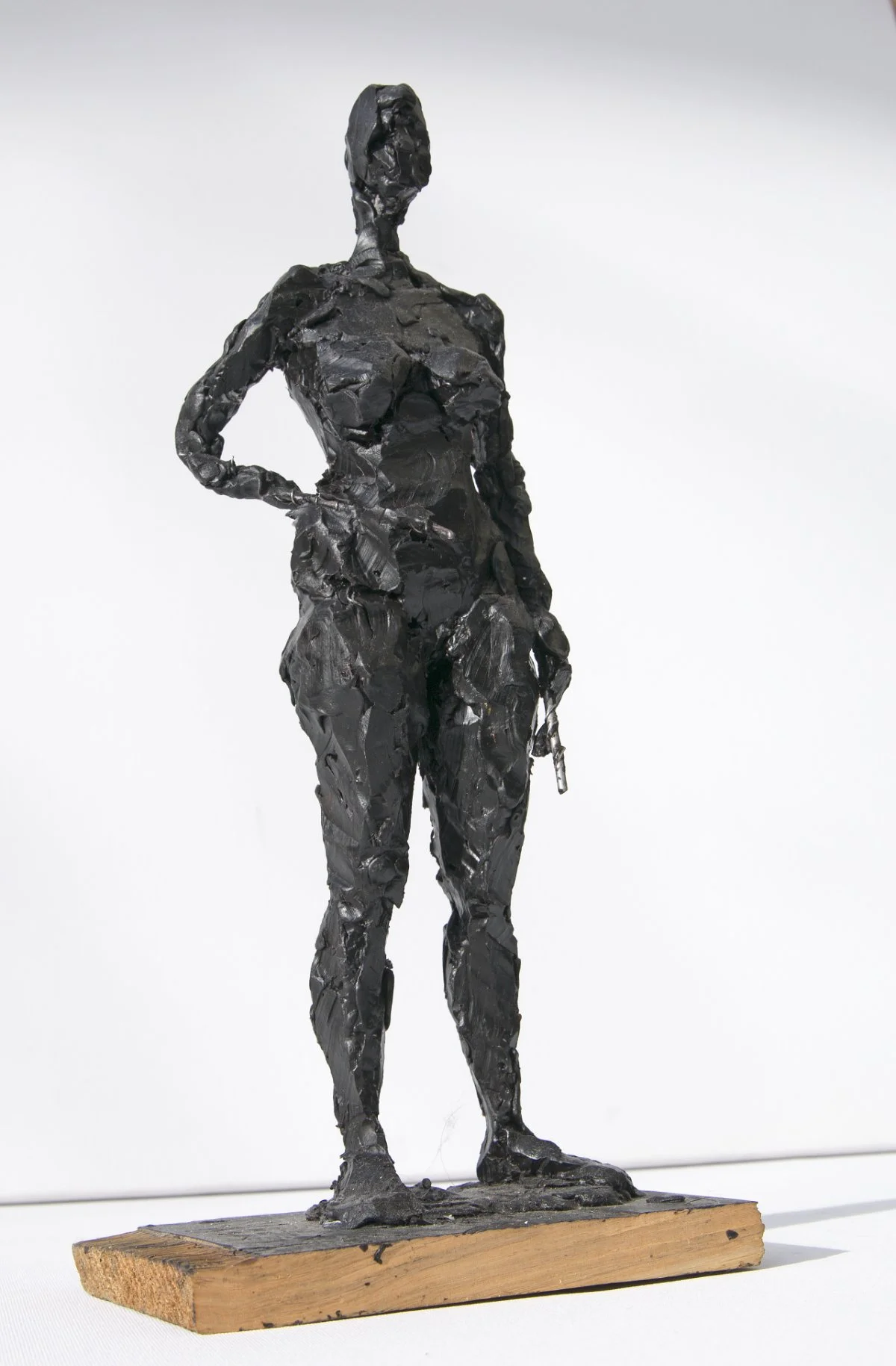 Eine schwarze Skulptur einer stehenden Frau mit einer Hand in der Hüfte, montiert auf einem Holzsockel.
